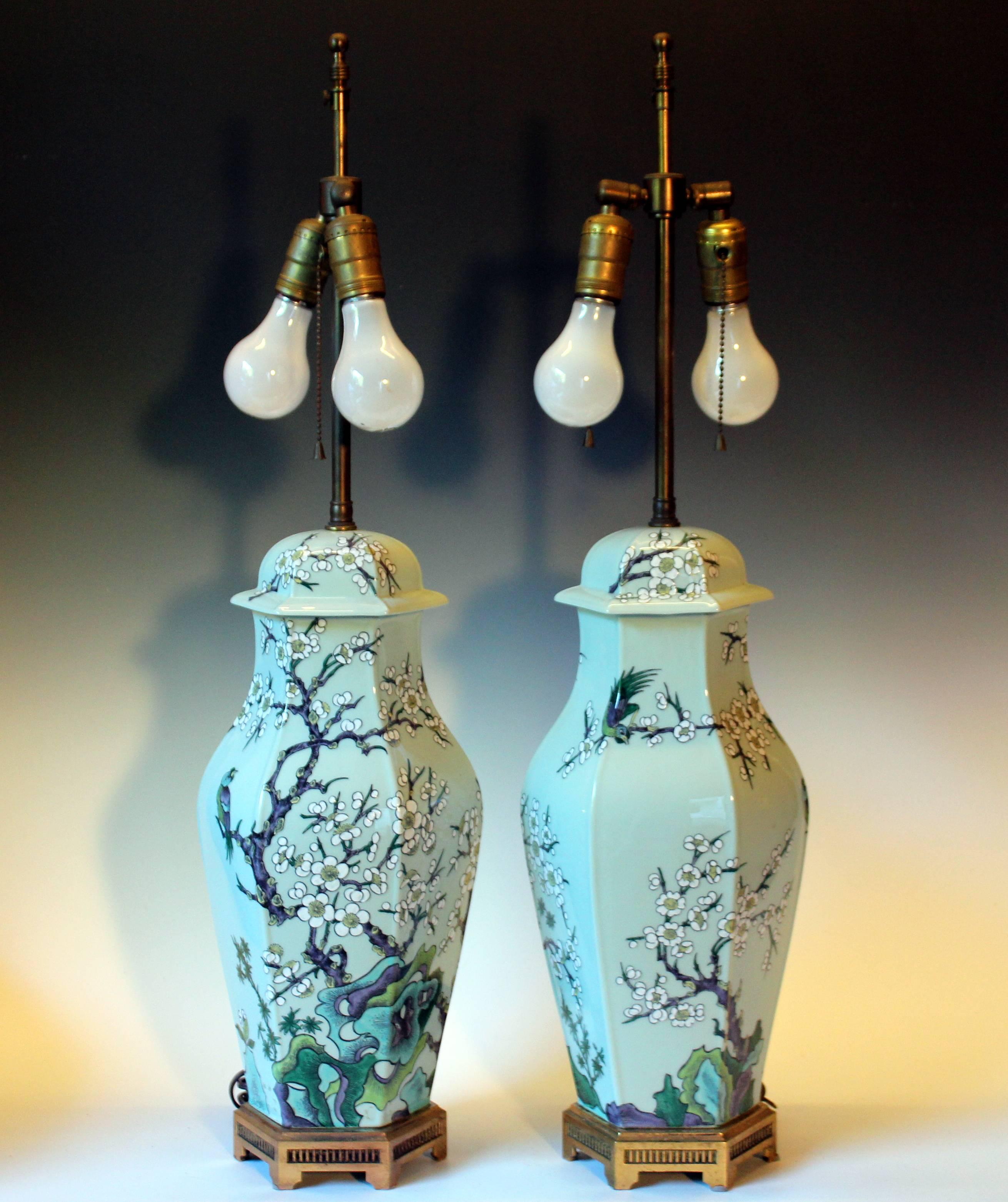Large pair of Paul Hanson porcelain lamps with chinoiserie decoration depicting rock outcroppings, plum blossoms, and song birds against a pale celadon ground, circa 1960s. Nice quality brass hardware with double cluster articulated sockets and