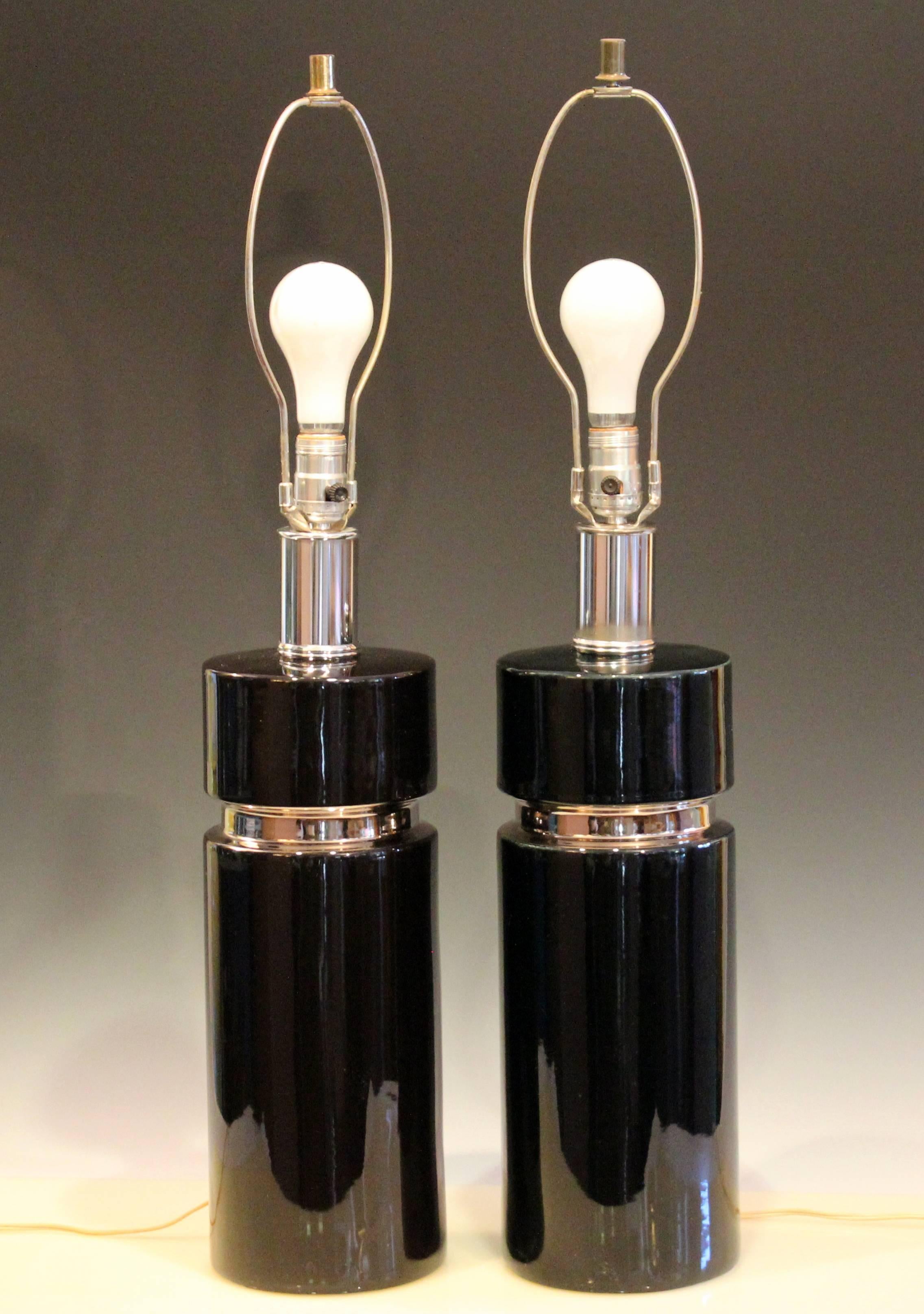 Pair of sleek vintage pottery lamps in gloss black glaze with platinum accents, circa 1970s-1980s. Measures: 34" high overall, 19" to socket, 6 1/2" diameter. Three way switches. Excellent vintage condition.