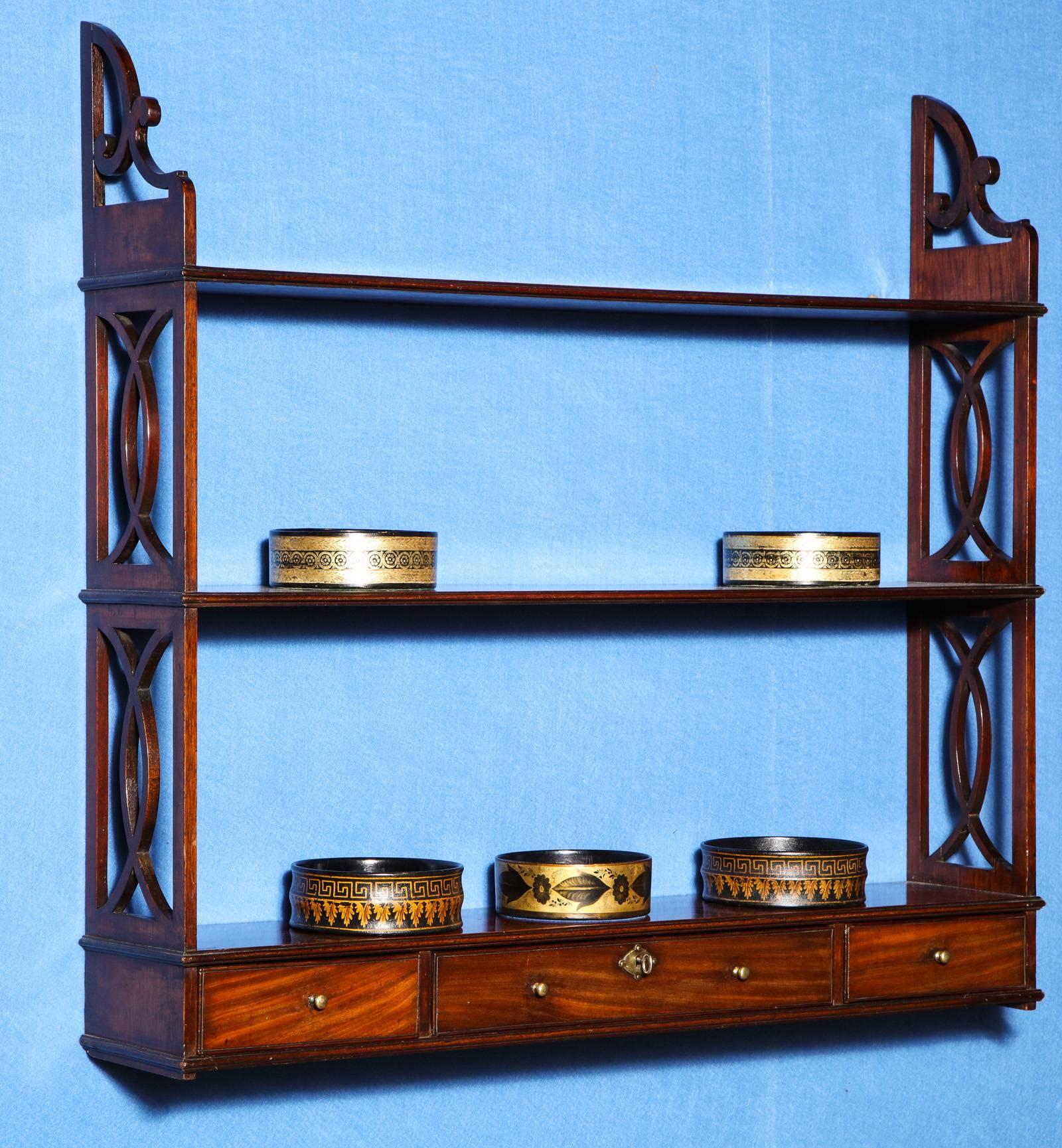 A finely figured set of Chinese Chippendale period carved mahogany hanging shelves, having pierced scrolled and fretwork supports joining three shelves, above three mahogany-lined drawers with original brass knobs, lock and escutcheon, one drawer