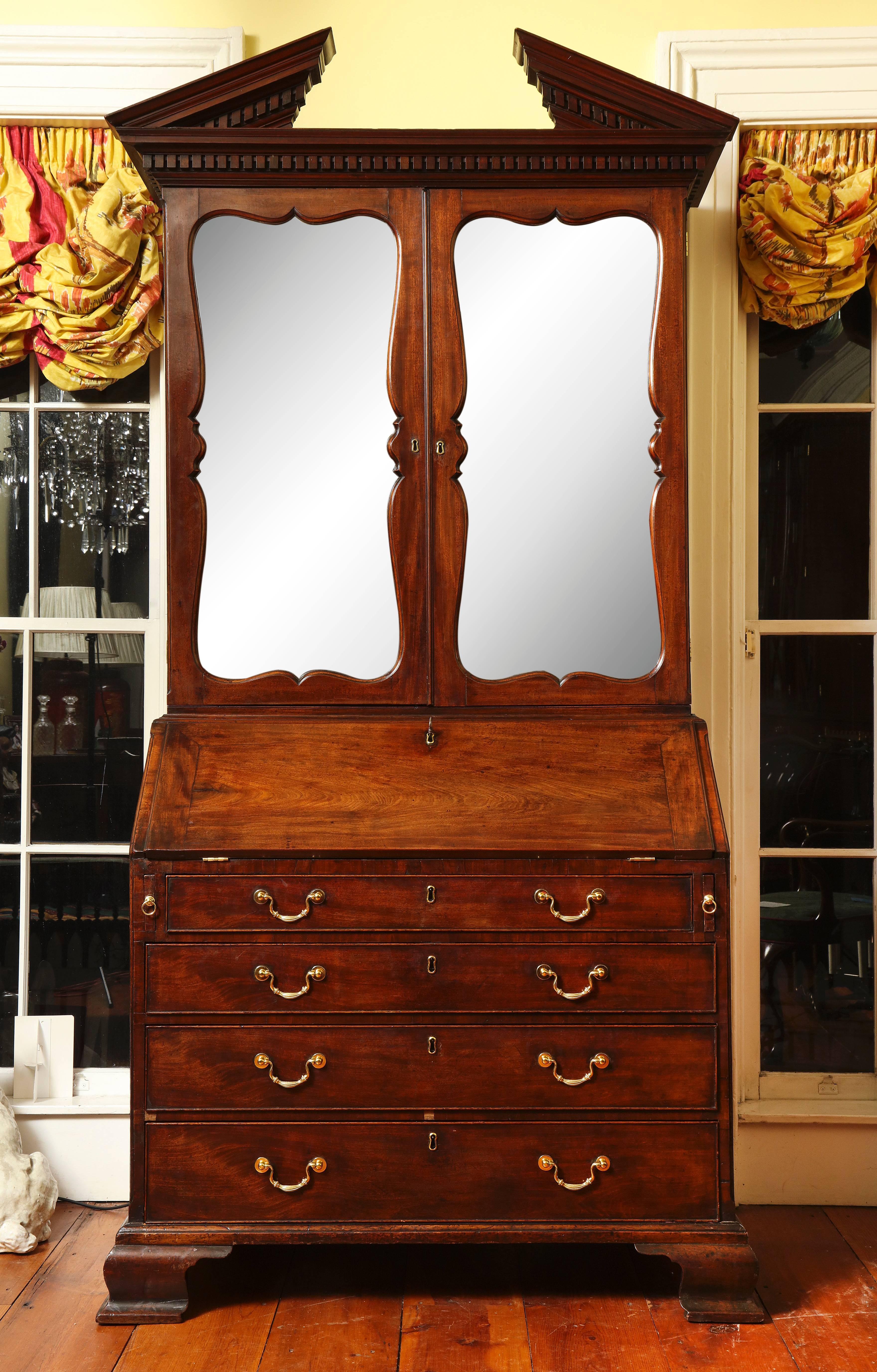 A very fine George II mahogany bureau bookcase attributed to Giles Grendey, the molded stepped cornice with dentil ornament below a similarly molded and ornamented broken pediment, the two doors below inset with mirror plates within shaped frames