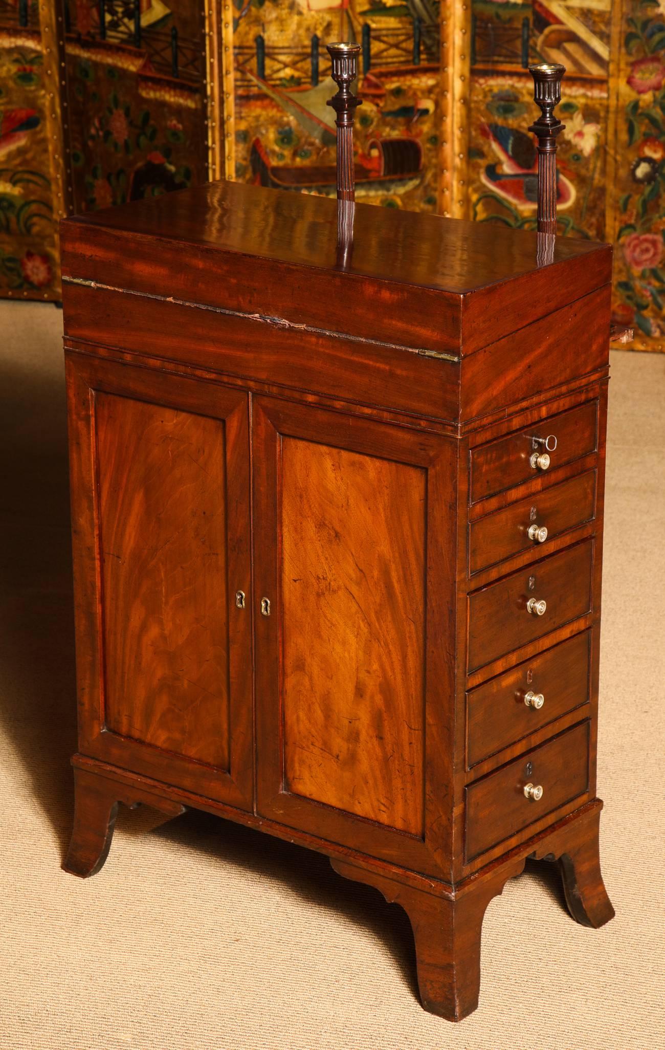 A rare Regency mahogany davenport desk, having a hinged top opening to reveal a leather-lined slanted writing surface with two hinged hidden compartments. The case designed as a double sided cupboard with faux doors. The sides alternating with one