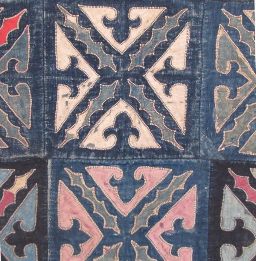 Mid-20th century Chinese minority (Miao) coverlet for a child with a patchwork of indigo blue squares joined together and decorated with geometric and foliage patterns of appliqued cotton in shades of dark & light indigo blue, pink and red.