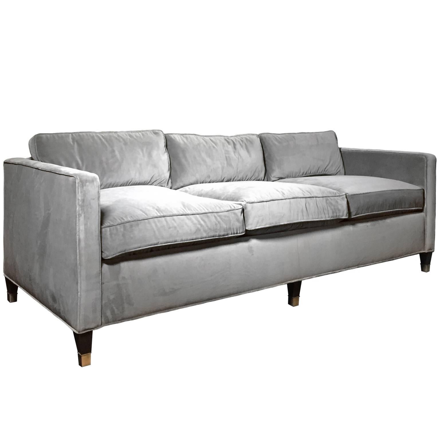 Custom three-seat sofa upholstered in grey velvet with tapered wood legs and brass sabots.