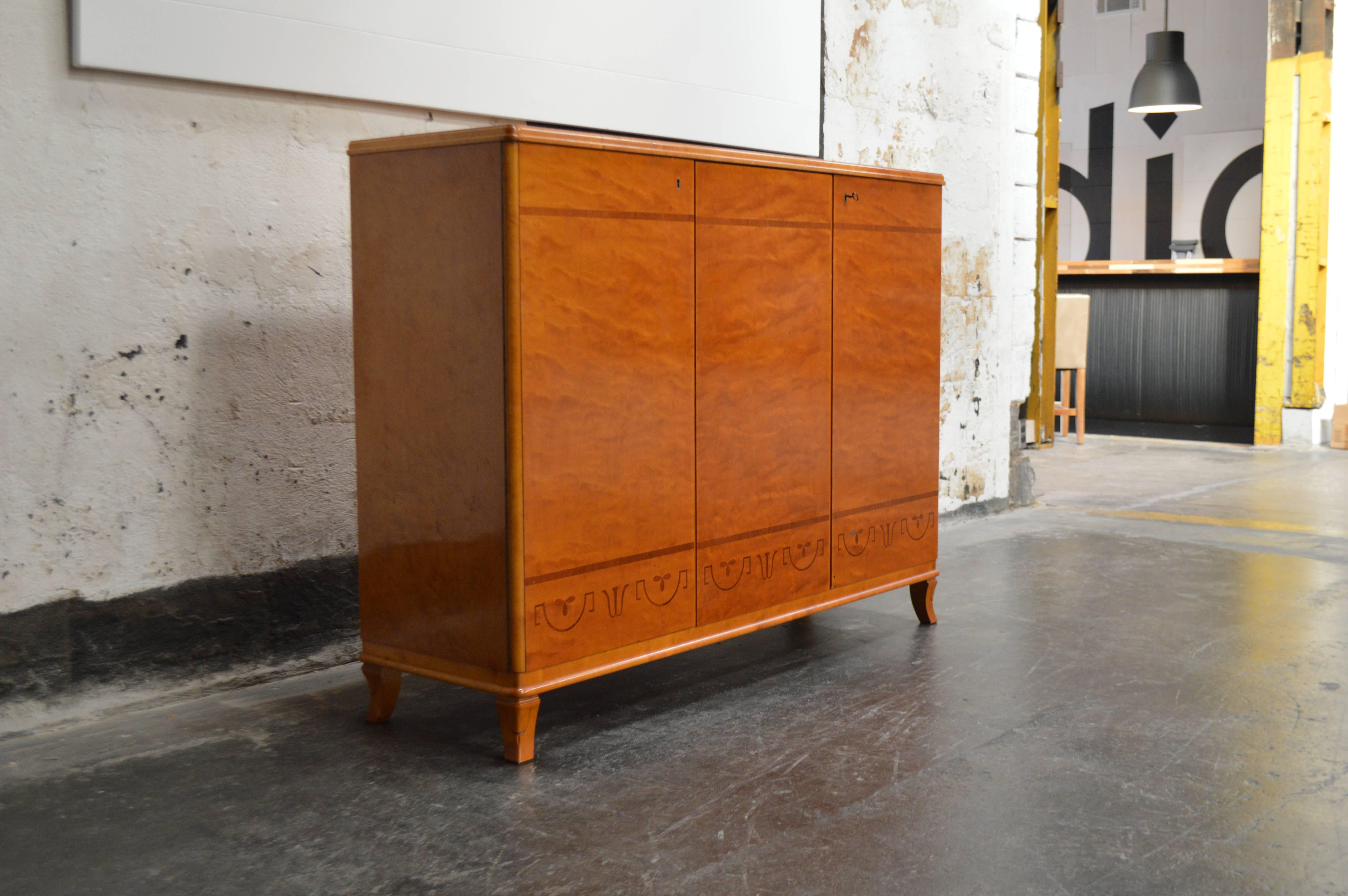 Art moderne cabinet crafted of native burped golden elm with inlay of light elm. This gorgeous wood has mellowed to a rich amber color. This storage piece opens to reveal an interior with deep shelves and has three drawers on the right. Key