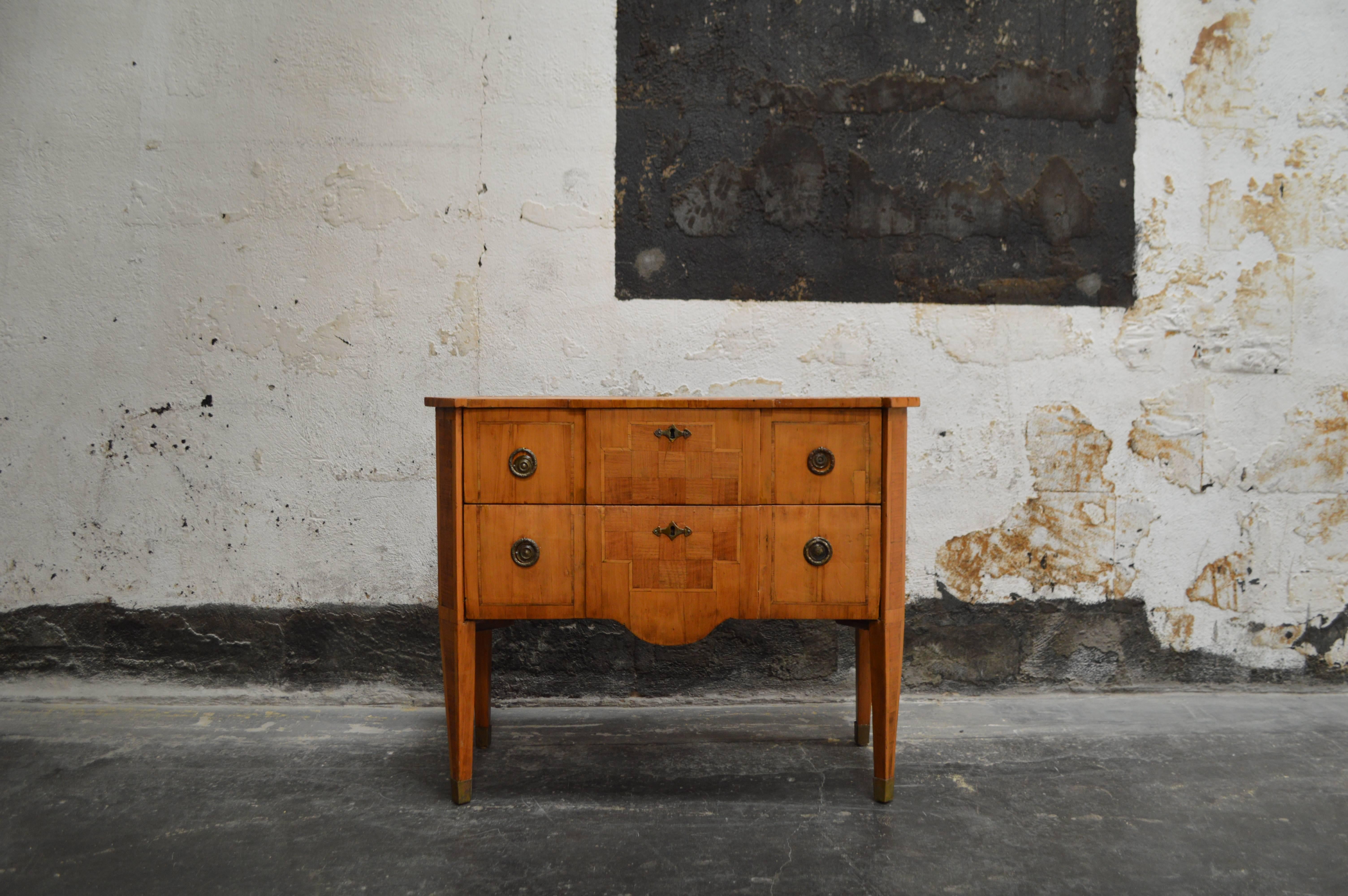 Handsome tailored Swedish chest inlaid parquetry and round Gustavian style pulls. It has been sealed but any natural cracks or patina have been kept and preserved. Two solid drawers atop tapered legs with brass cup details. Functional beauty as a