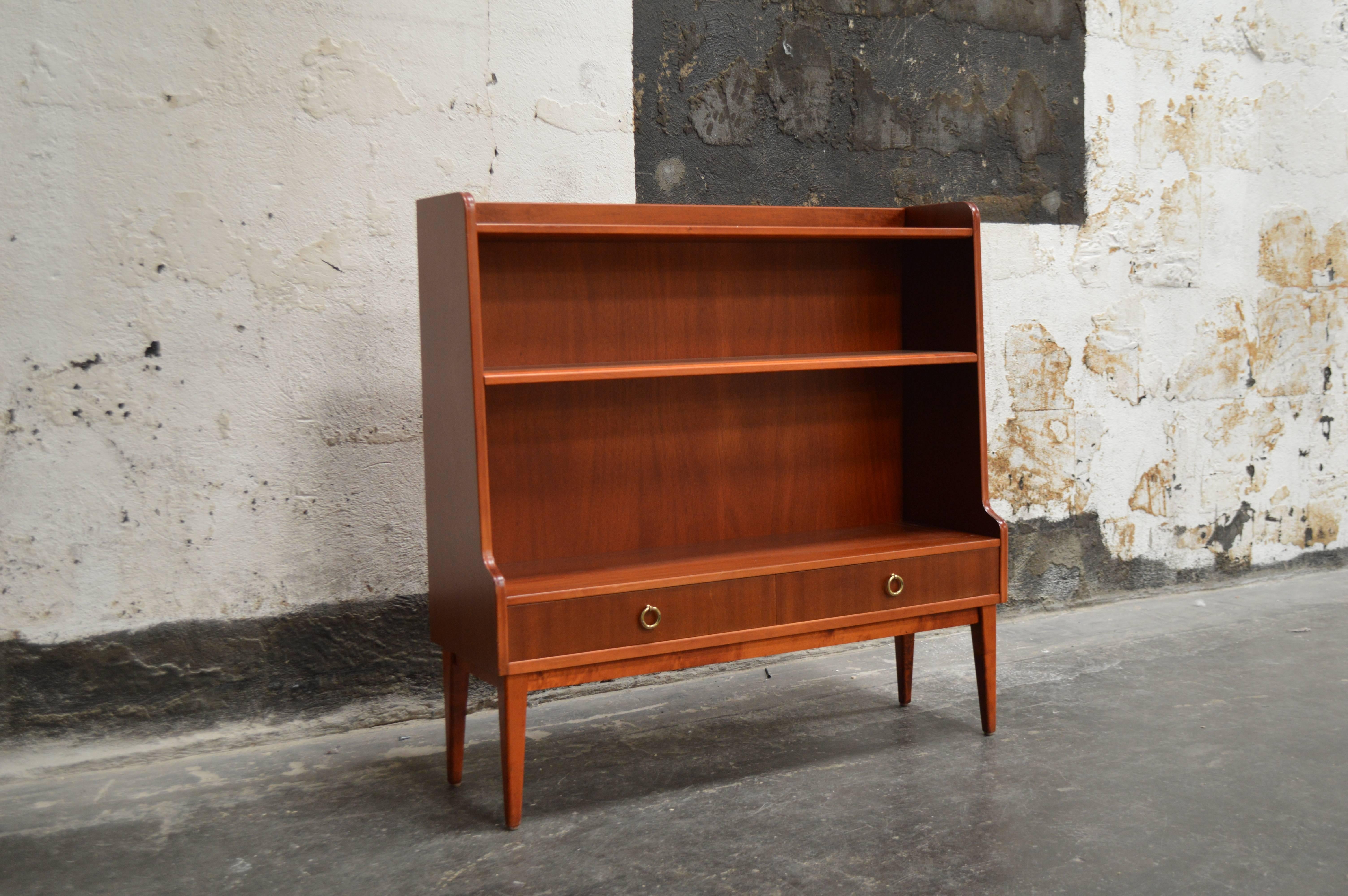 This exceptional Mid-Century bar or bookcase features open shelving for display of barware or accessories, the lower half has two drawers with original brass ring pulls. This petite piece packs a lot of punch and is perfect for any small space.