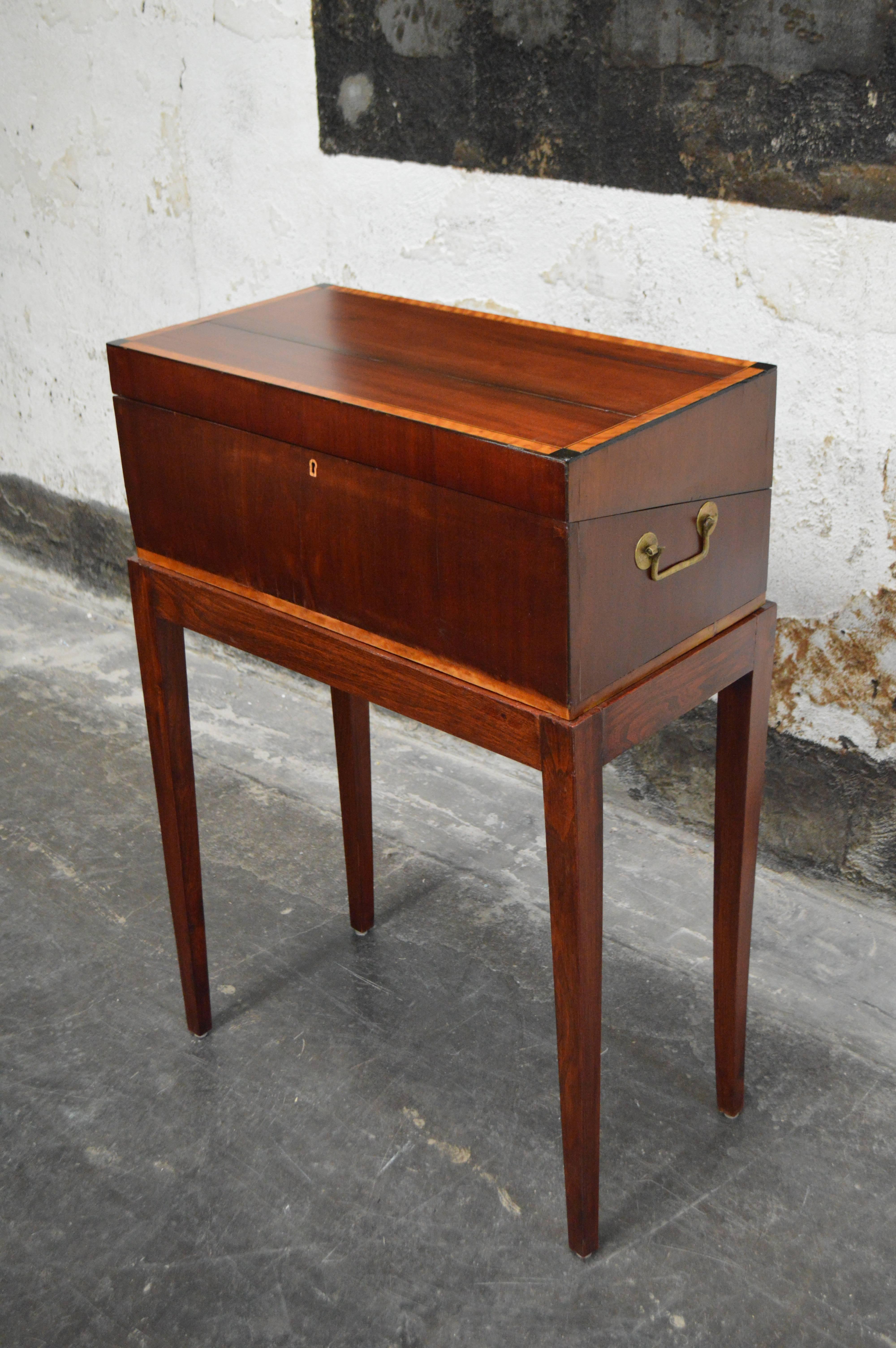 Antique mahogany intarsia writing box or lap desk on rosewood stand. Opening it up reveals a dished pen tray flanked by space for inkwells. Beneath the writing slope is a small letter well. Brass handles adorn the sides and also has a drawer section