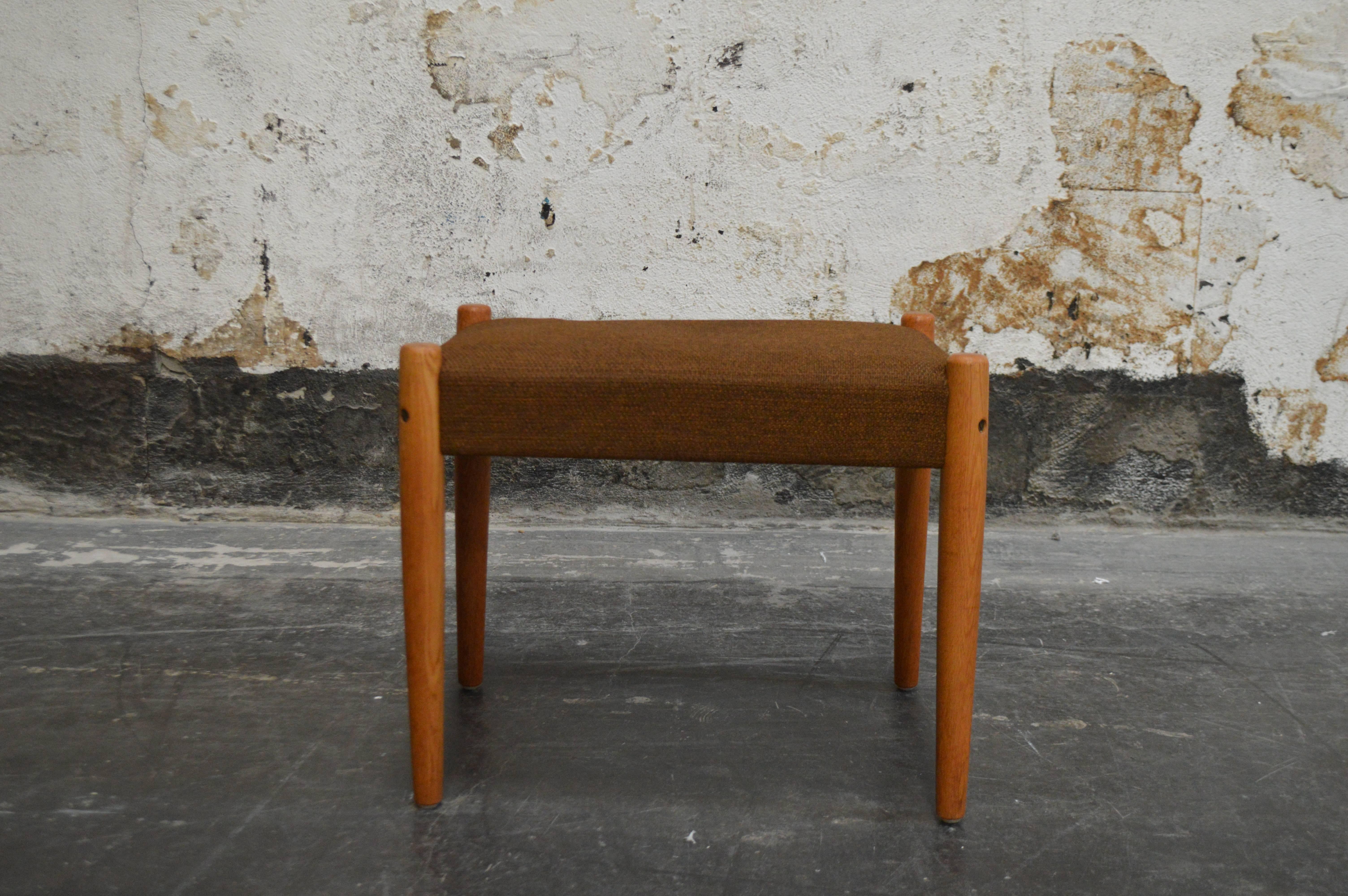This vintage Danish modern footstool features sturdy teak legs with original brown tweed upholstery. Can be reupholstered in any COM fabric. This handsome stool makes a sturdy and stylish addition to any interior.