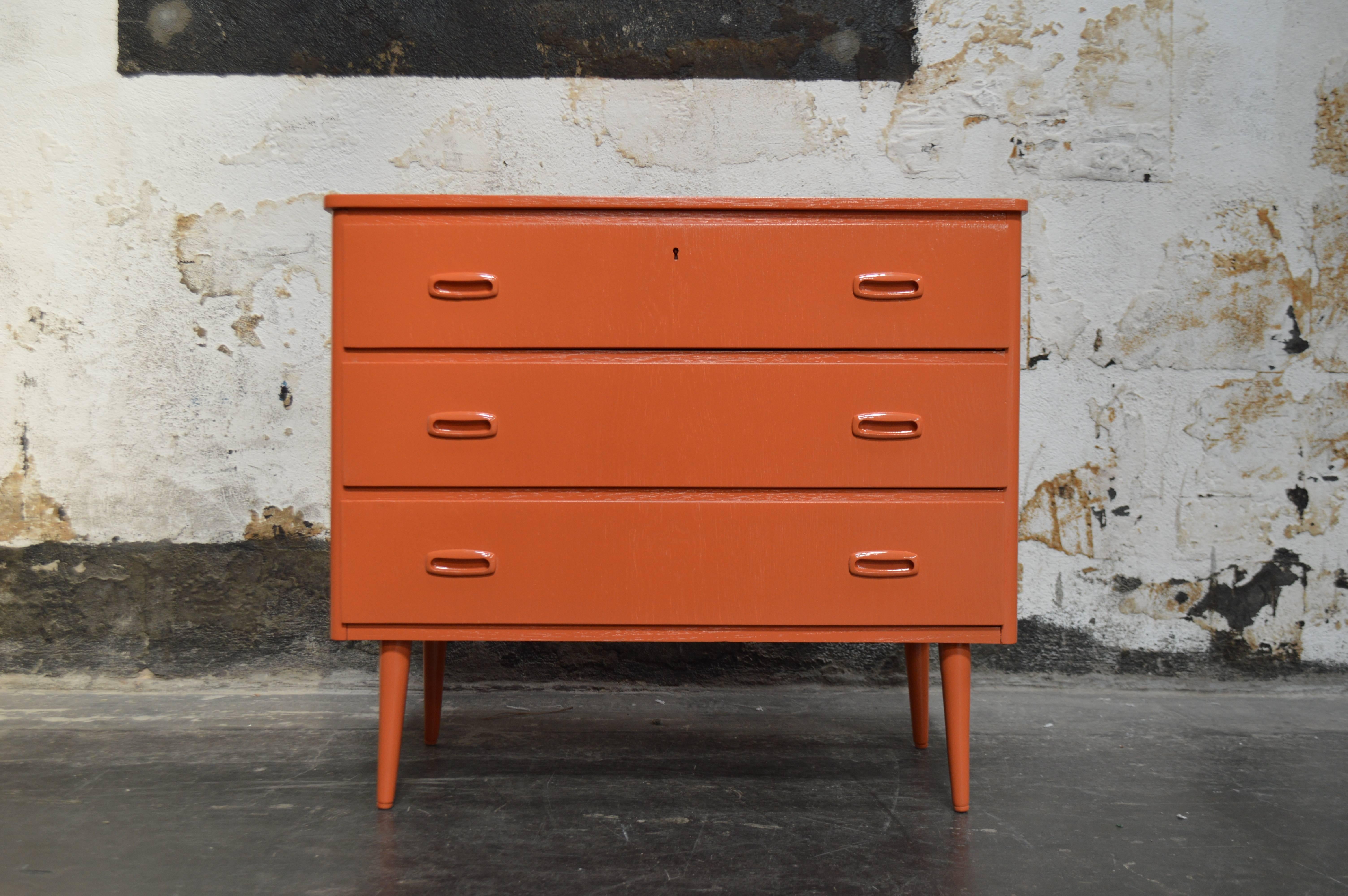 Mid-Century Modern three-drawer teak chest newly refinished in shiny dark orange lacquer on round tapered legs with original inset pulls.

A great piece to store your bedding or clothes. Works really well as a nightstand. A handsome piece of