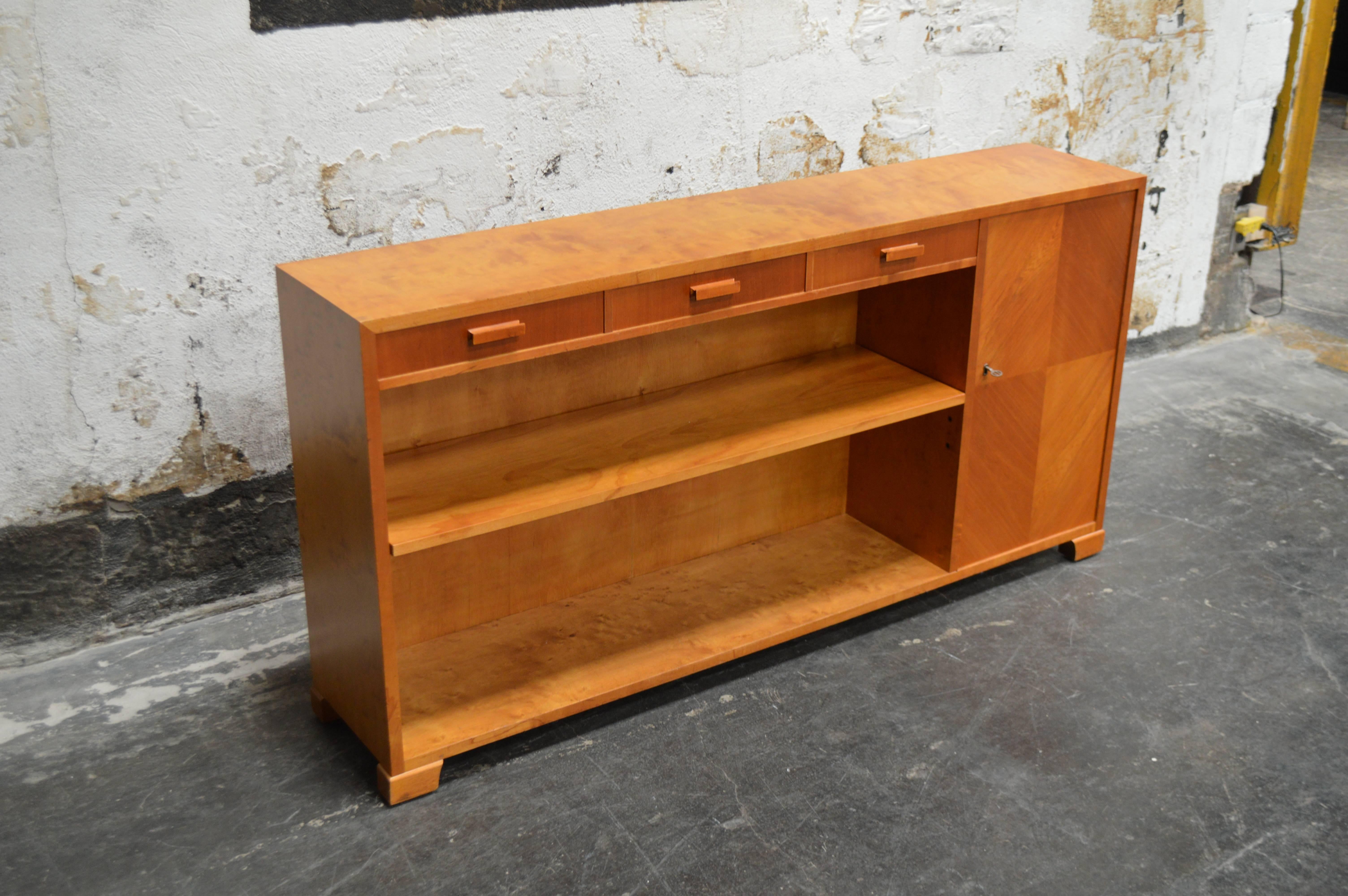 Art Deco or Art Moderne bookcase was cabinet crafted of native golden elm with bookmatched door. This gorgeous wood has mellowed to a rich amber color. Adjustable shelves. Key included. Perfect as a slim console or stand for a flat screen TV.