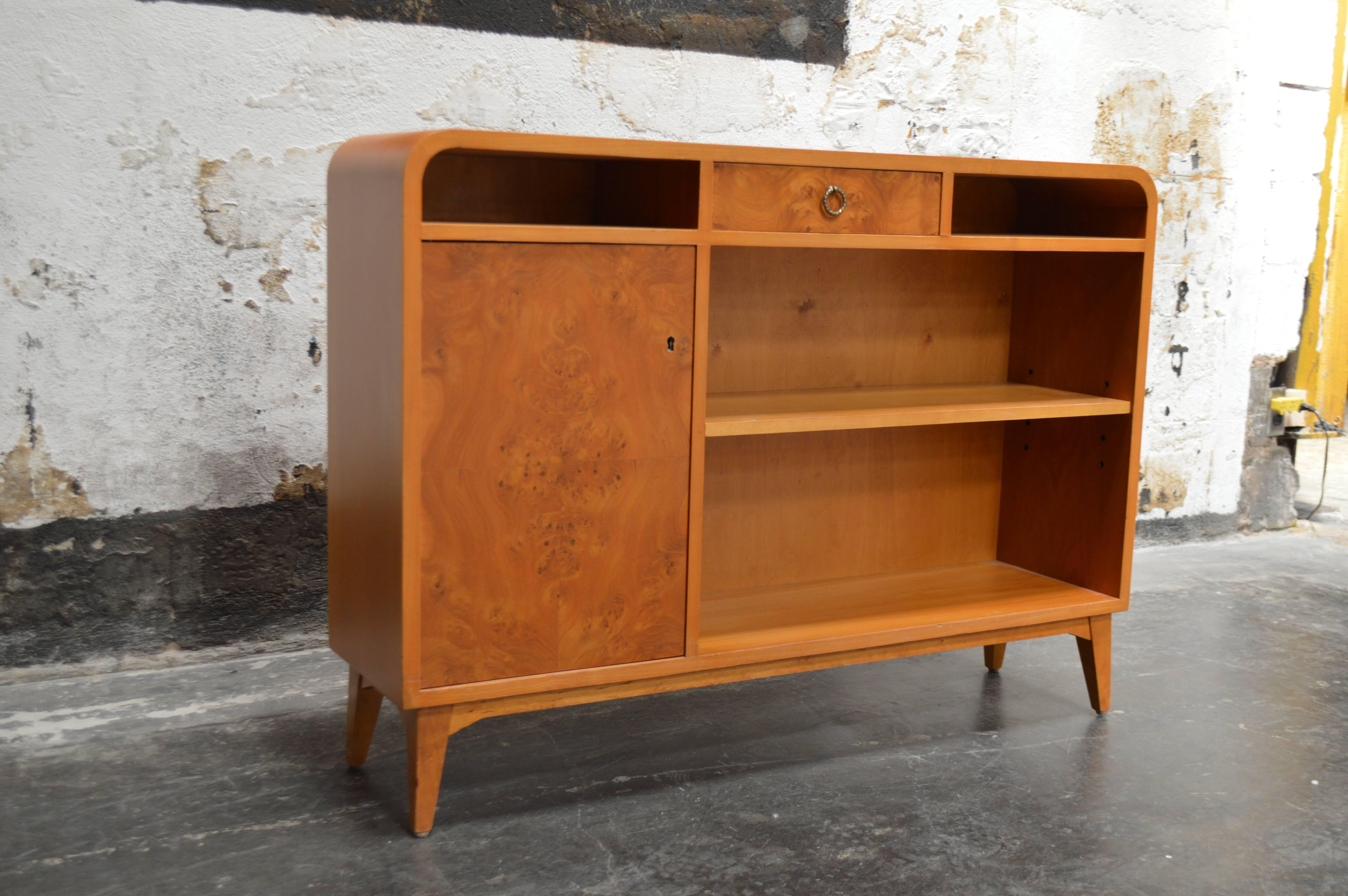Mid-Century or Art Moderne bookcase was cabinet crafted of native golden elm with Carpathian elm door and drawer. This gorgeous wood has mellowed to a rich amber color. Adjustable shelves. Key included. Perfect as a slim console or stand for a flat