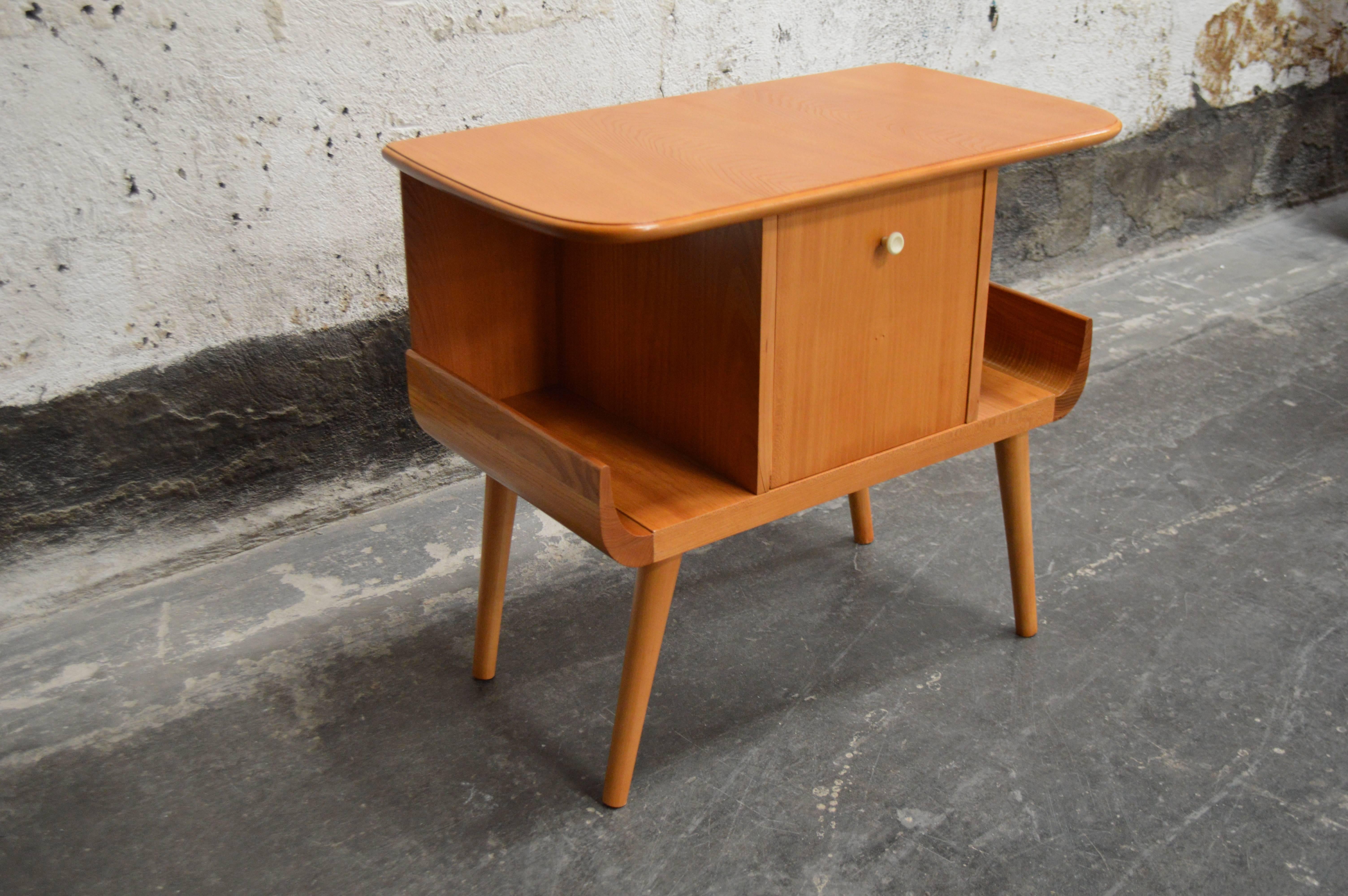 Unique Swedish Mid-Century side table crafted of golden elm features open side winged shelves with a storage cabinet in the center. Great petite piece with lots of style. Castors can be added to the legs to make this a rolling table or small bar