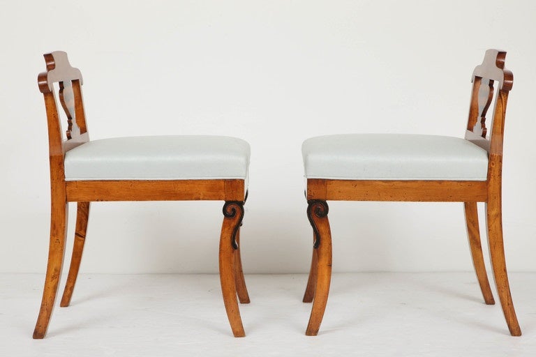 A pair of Swedish Karl Johan birchwood and ebonized stools with neoclassical penwork, Circa 1830, each with a single arm classically decorated baluster form splat, upholstered seat raised on sabre legs headed with ebonized scrolls. Both with a