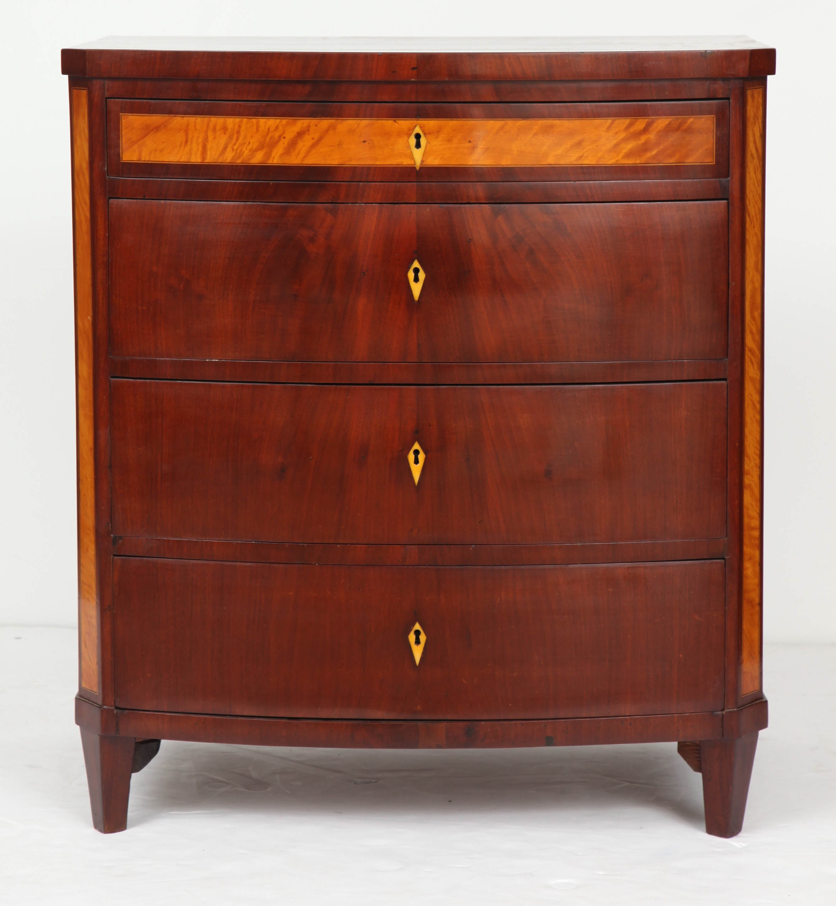 A Danish Empire mahogany and fruitwood commode, circa 1820s, the rectangular top with a bow-front and canted corners above four conforming drawers and fruitwood canted sides, the top drawer with a fruitwood inlaid panel, raised on square tapered