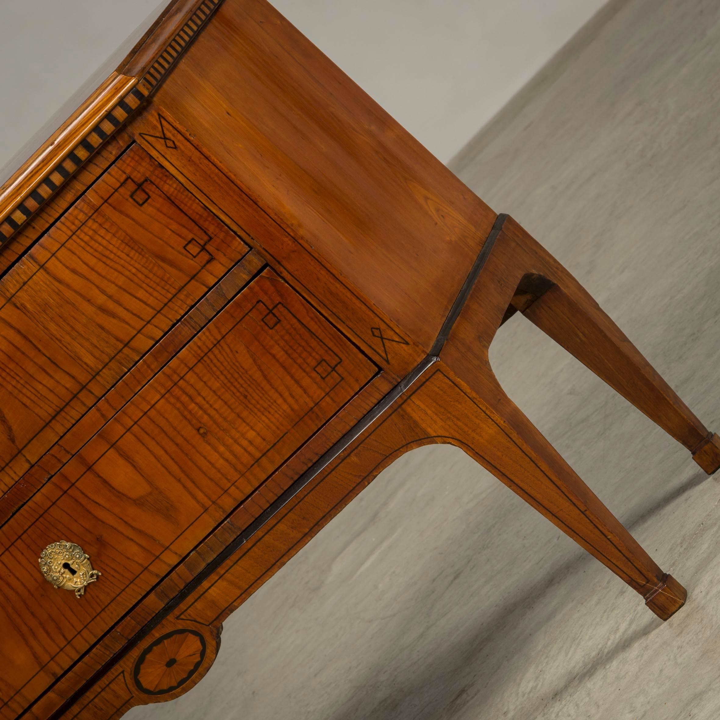 A Danish Louis XVI elm and inlaid commode, late 18th-early 19th century, the rectangular top with a molded edge above a dentil molded frieze, with two long drawers bordered with line inlay and with a lower inlaid fan medallion, raised on square