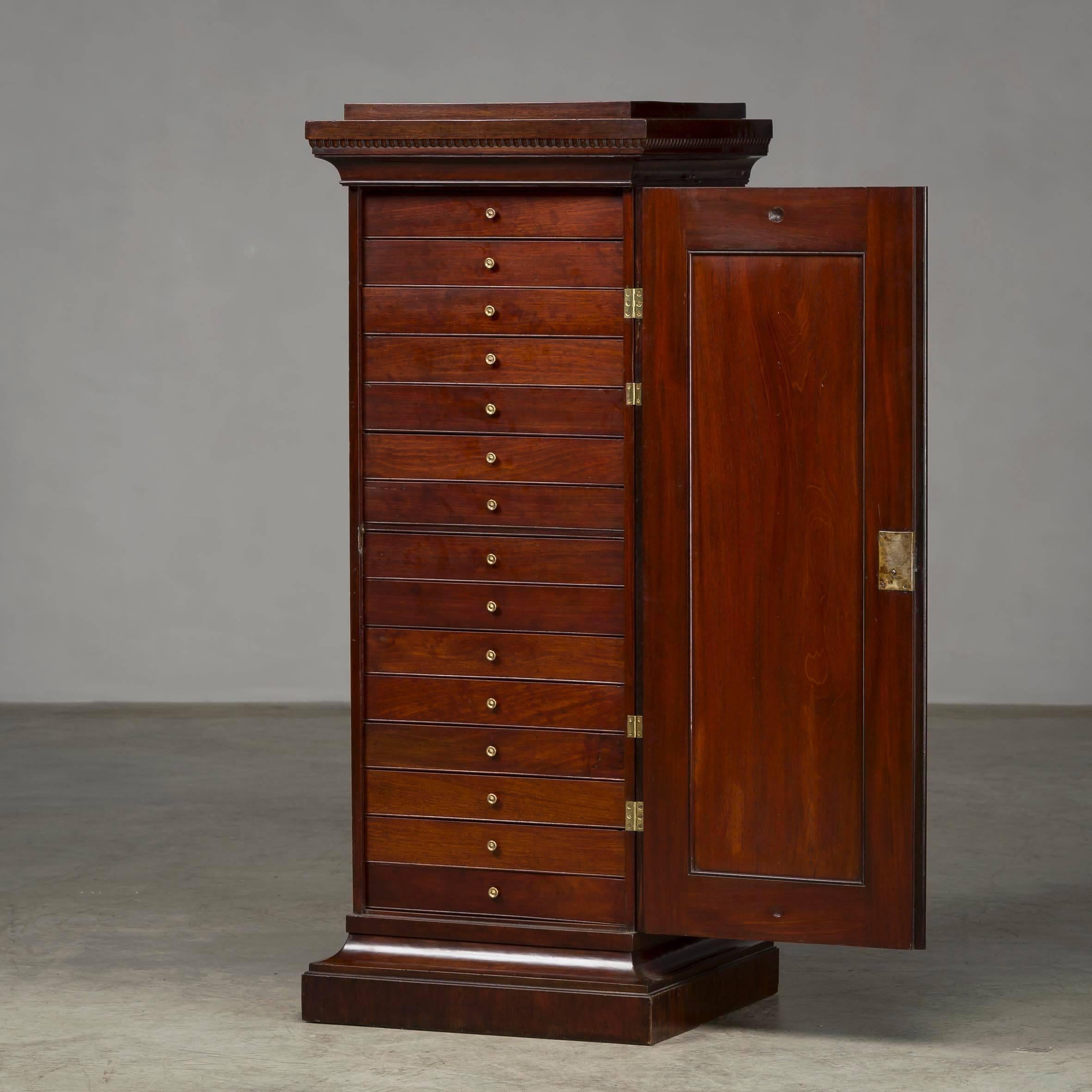 A Danish Louis XVI mahogany pedestal storage cabinet, circa 1790s, with a rectangular stepped top above a single paneled cupboard door with a recessed center circle, enclosing an interior comprising of 15 slim drawers, raised on a molded plinth