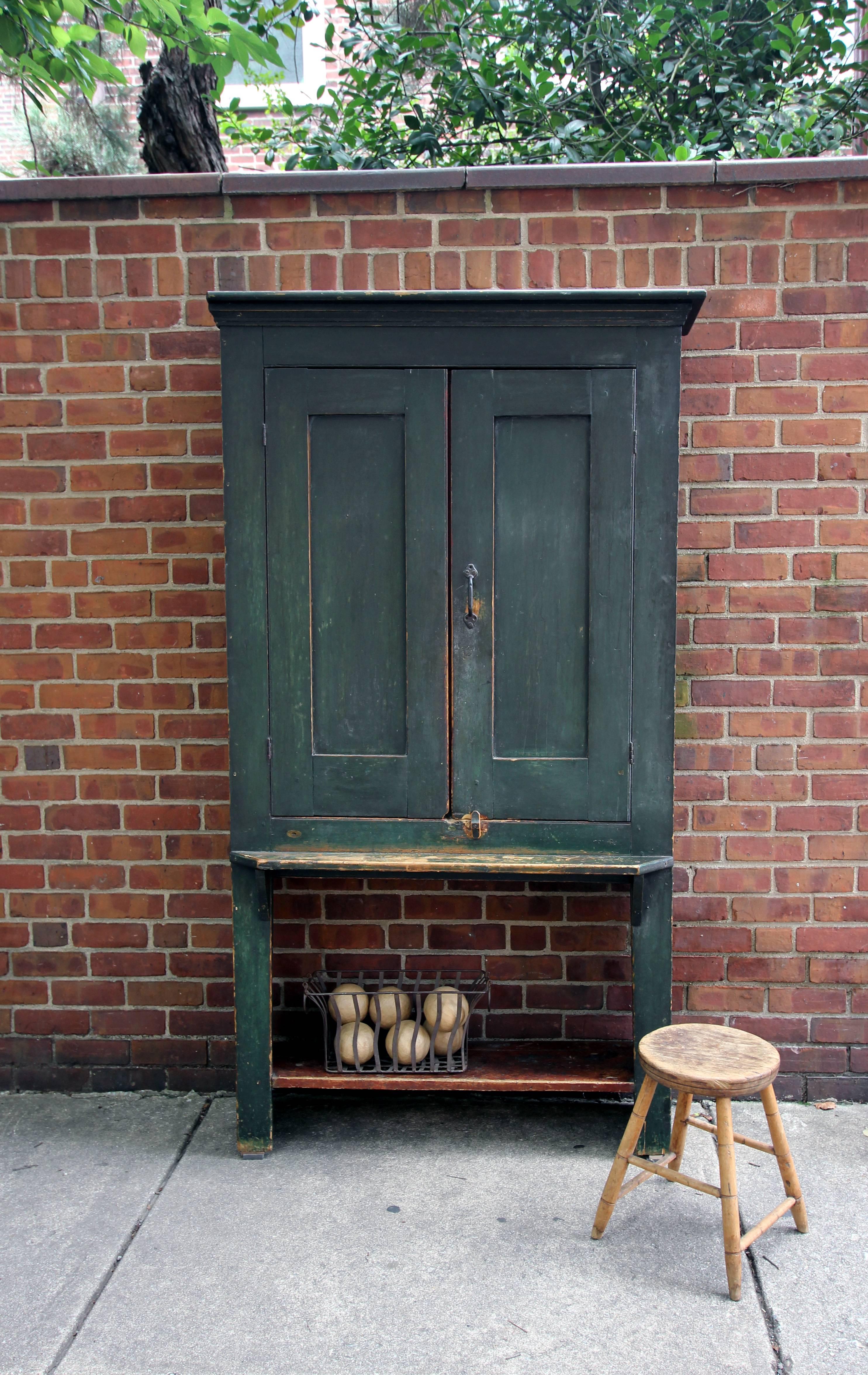 Tall, shallow cupboard of unusual and very handsome form in old green paint, strong lines, excellent wear, four interior shelves and one low shelf under the cabinet. Interesting mid height shelf as well, 4