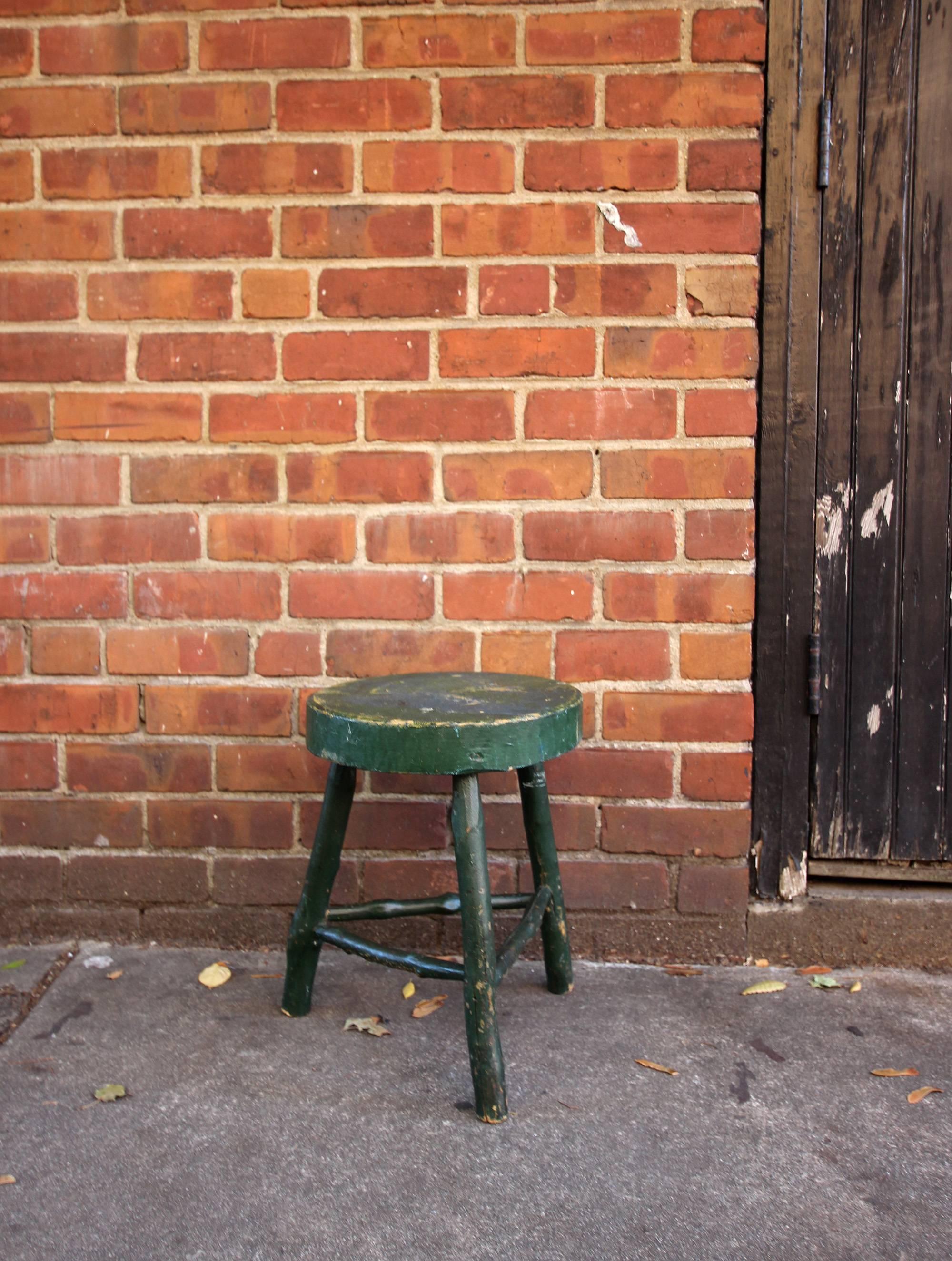 Low, fat tripod stool with a round carved seat and twig legs and stretchers, original green paint, American, circa 1890. Could be used as a stool for sitting or a small table. Very sturdy.