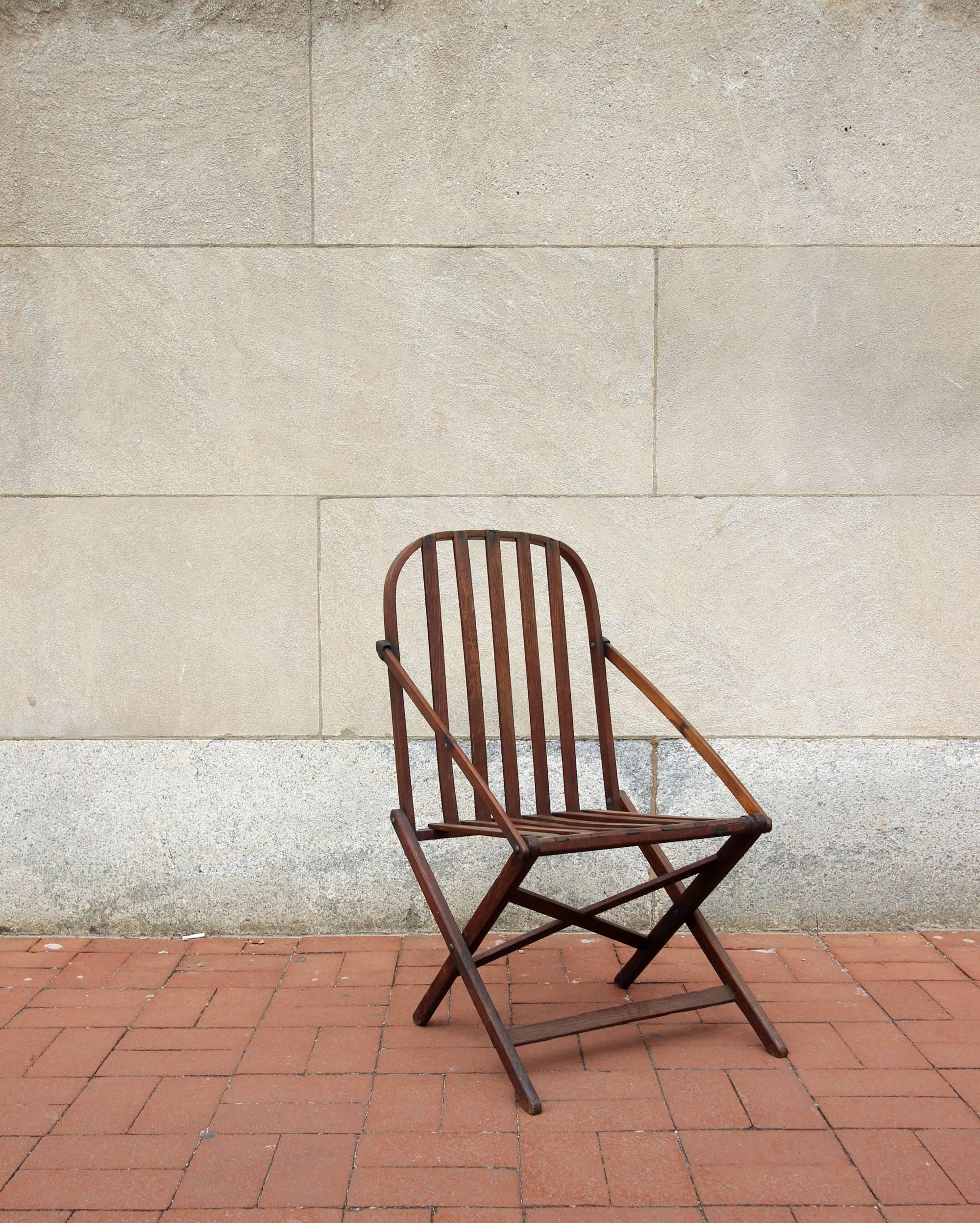 Sculptural and yet functional folding camp chair; on the smaller size and very portable. Walnut wood, American, early 20th century. Wonderful dry patina and color to wood.