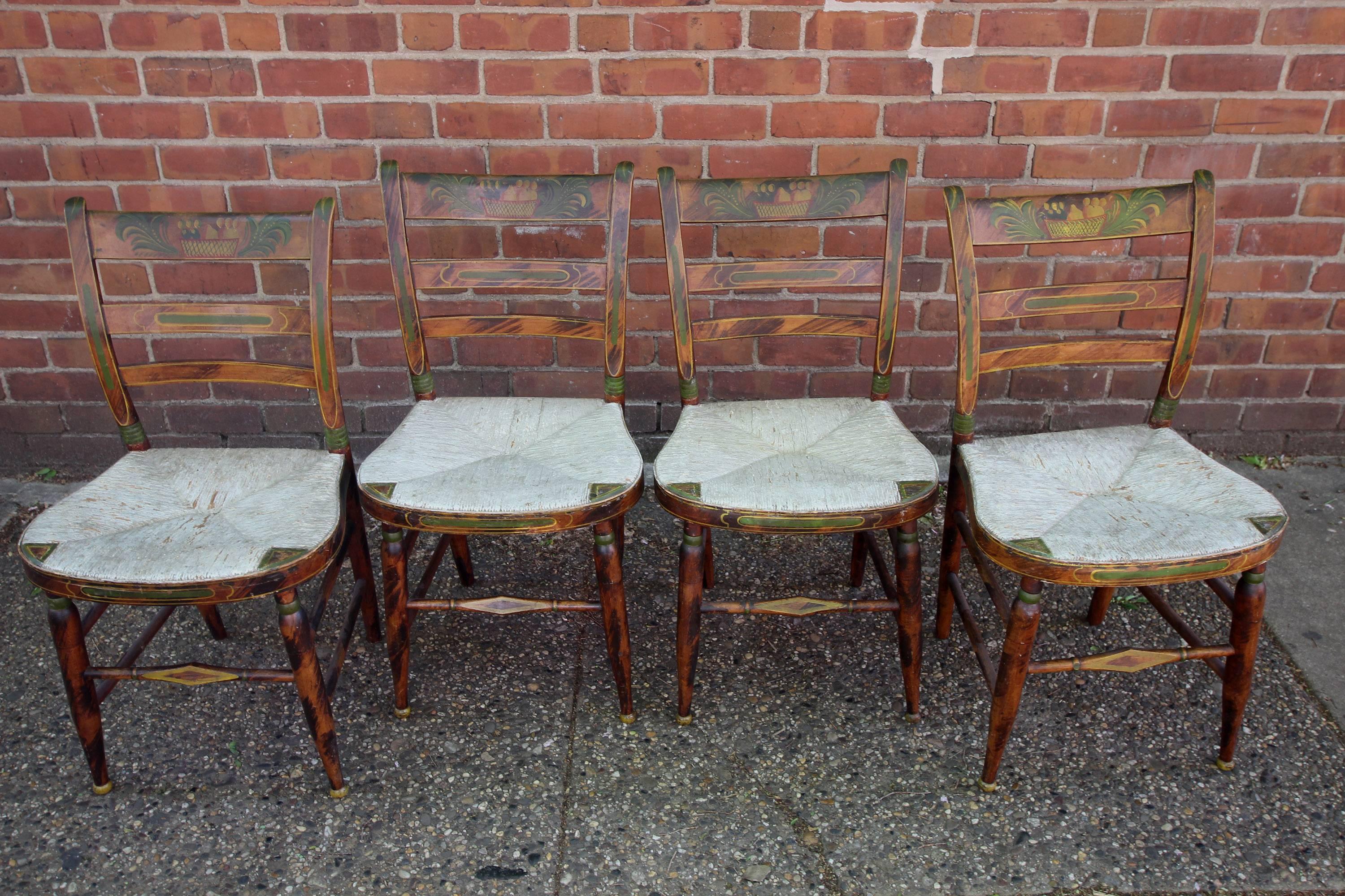 Six excellent paint decorated, rush seat dining chairs, four side chairs and a pair of armchairs all with painted free-form and stencilled fruit or baskets of fruit. The side chairs are all original, including their painted rush seats. The armchairs