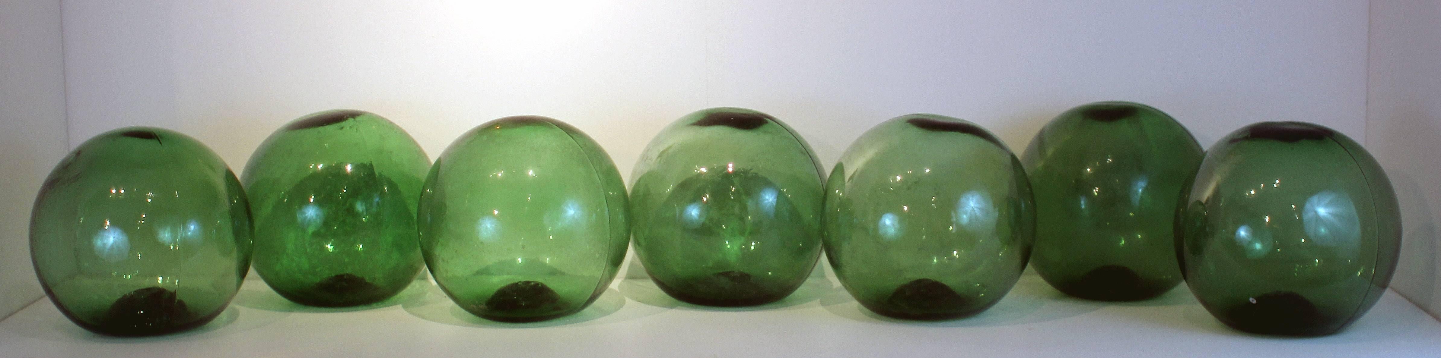 These 7 enormous glass balls were once used as floats in fishing nets in Maine. Blown and molded bright, deep green glass (all the same color). They each measure about 12" in diameter and sit flat. Sold only as a group.