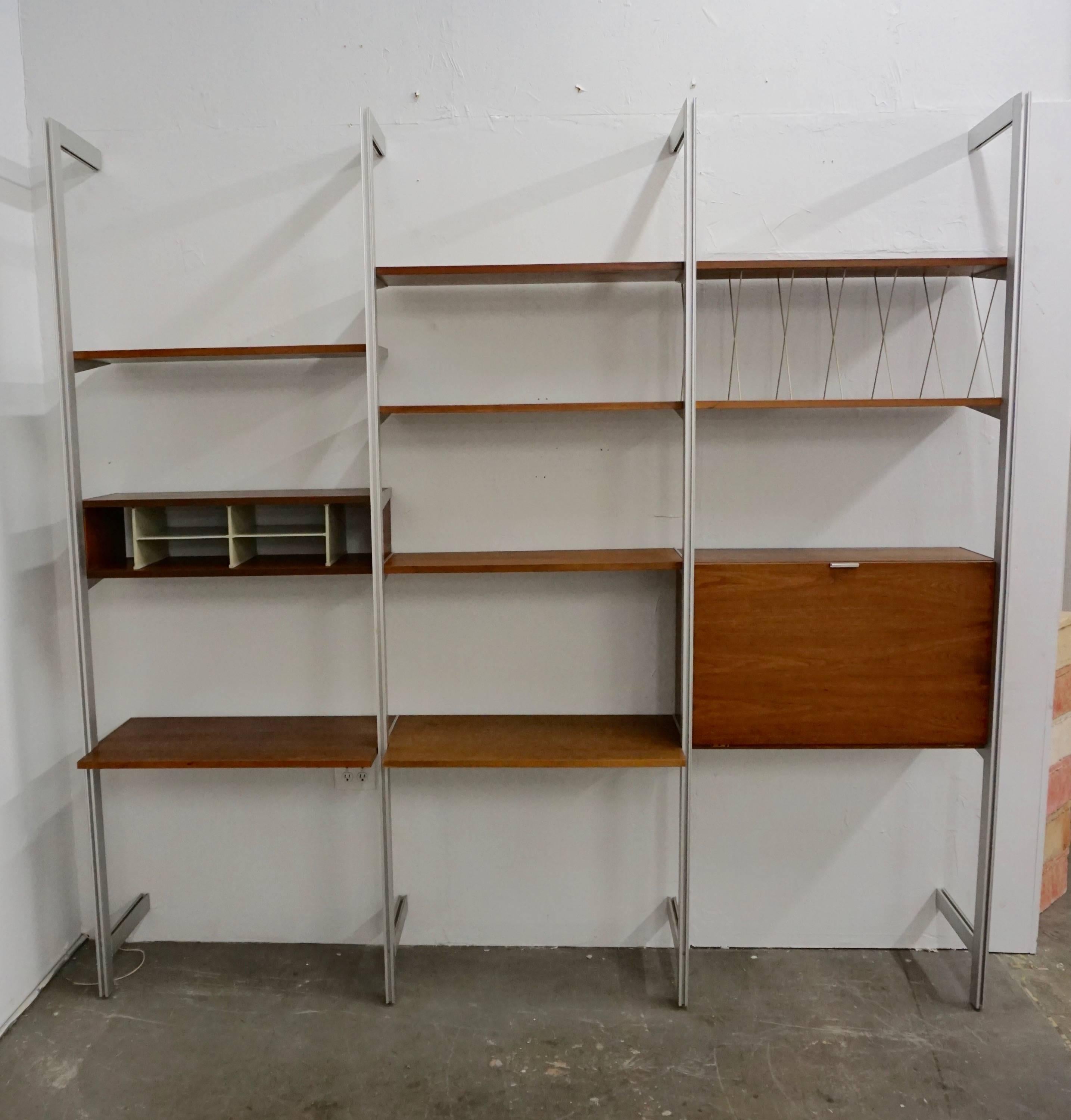 Manufactured by Herman Miller.
Consisting of:
Four aluminum poles with two crossbars each.
One drop down desk.
One record holder for LP's.
One slotted cabinet.
Six shelves.
Walnut veneered components.