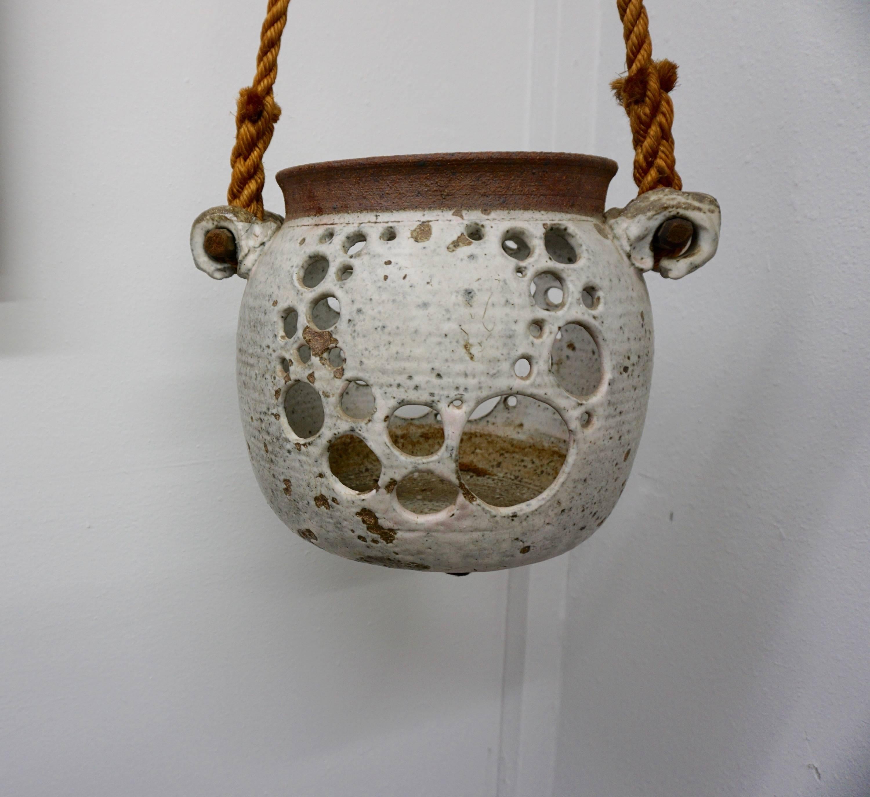 Stoneware vessel with multiple decorative holes hanging from rope attached to wooden rods. Illegibly signed at base.