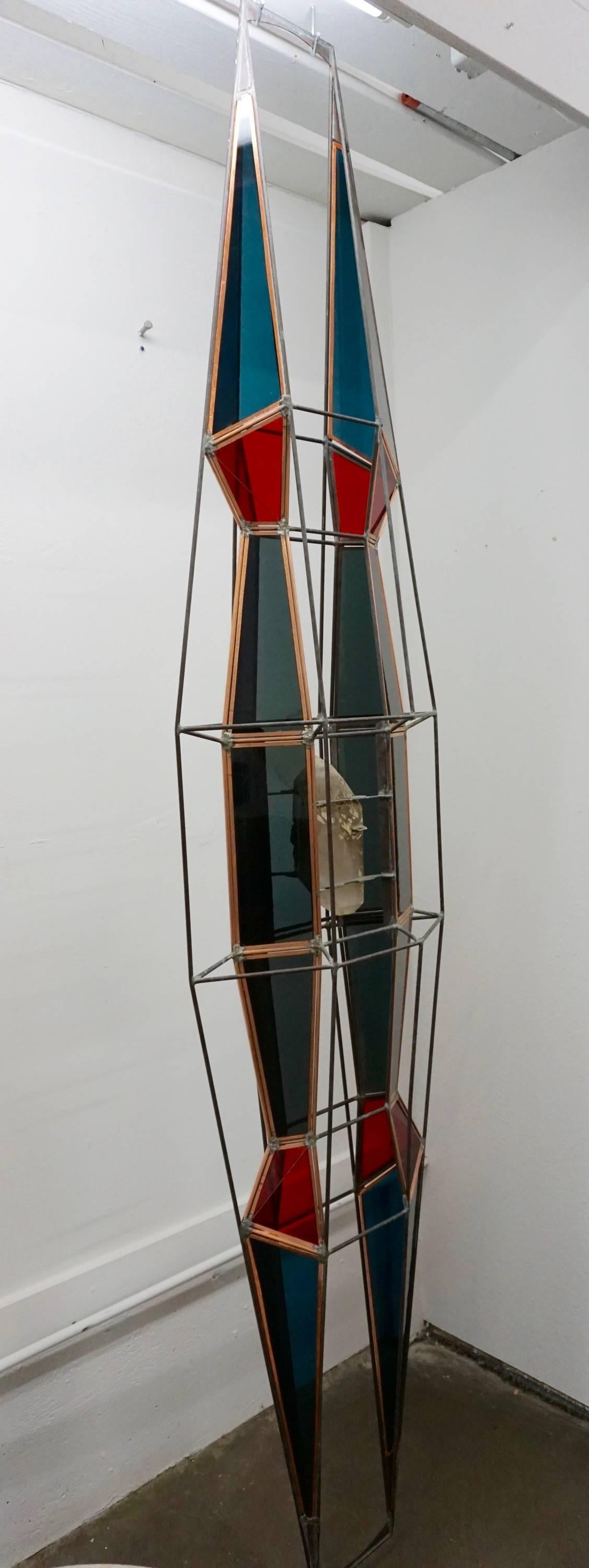 Handcrafted from steel rods with sections of stained glass in shades of blue and red. A piece of quartz crystal rests in the middle of the sculpture. Can be hung vertically or horizontally.