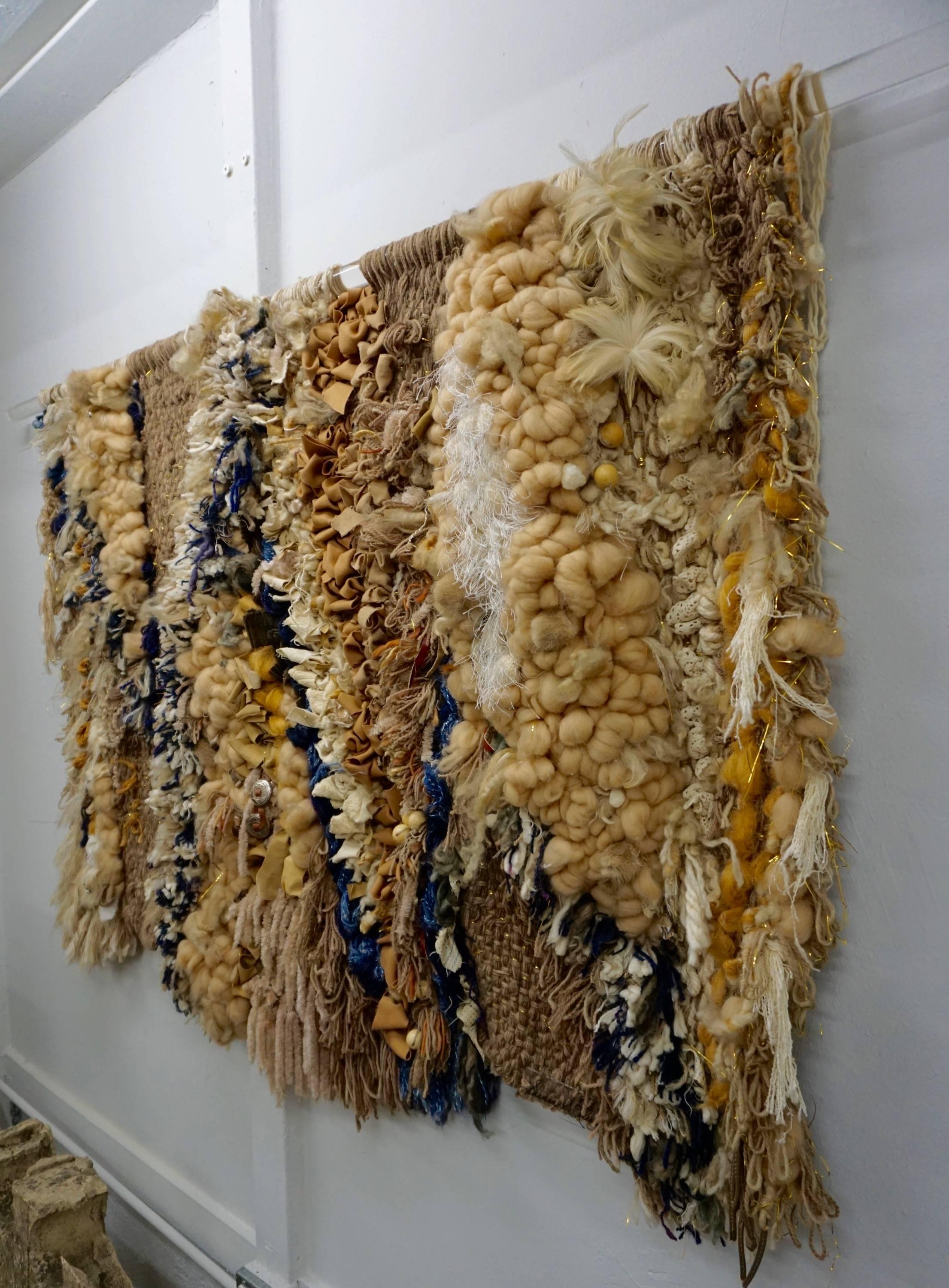 Highly textured with embellishments of leather, wood beads, feathers, lace, tufted wool, rope and conches. Signed by the artist on a piece of Lucite and hung on a Lucite rod.