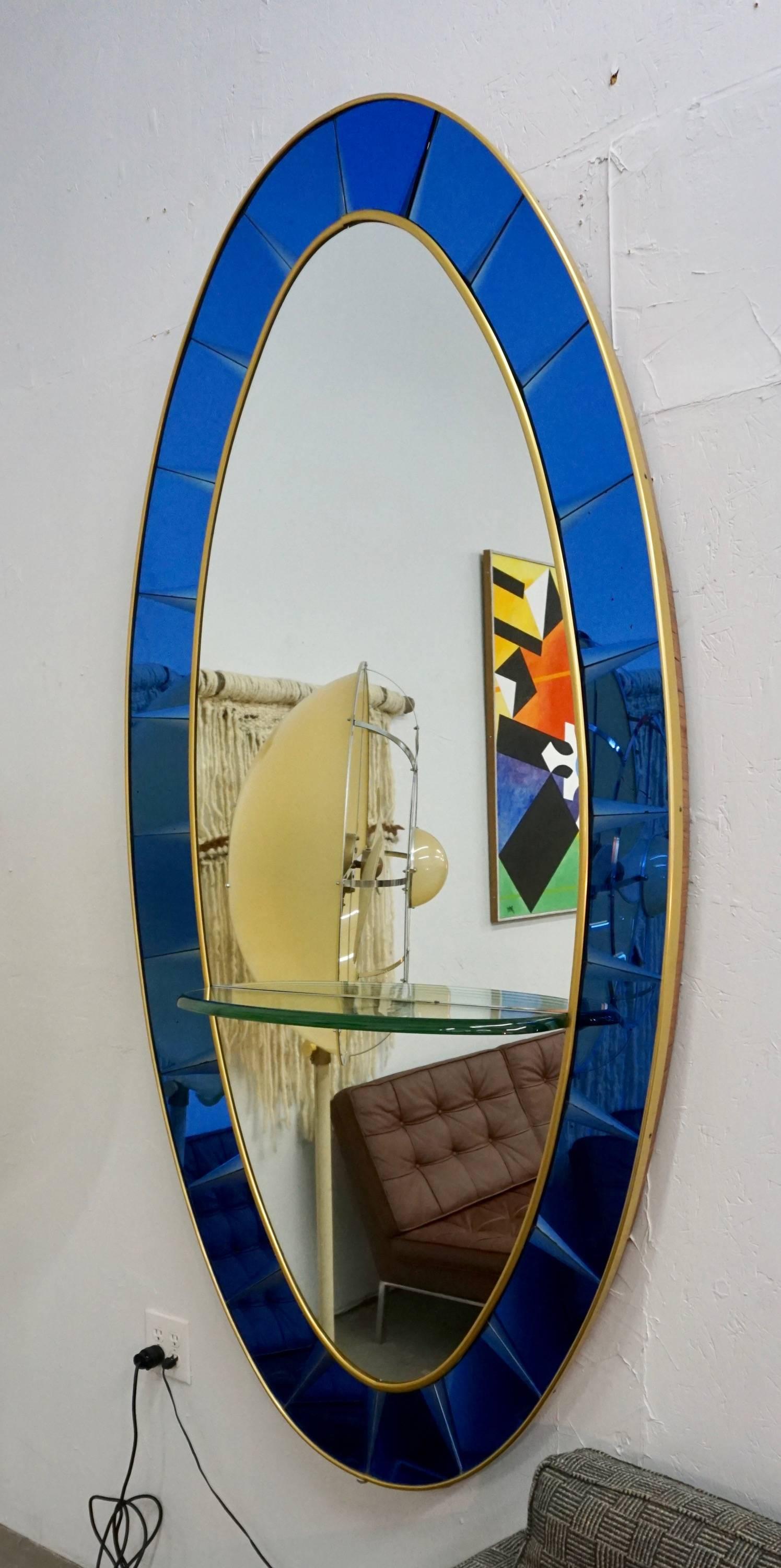 Beautiful large oval mirror, manufactured by Cristal Art, Turin, Italy.
The mirror is surrounded by beveled cobalt blue glass panels, placed in a gilt brass and wooden frame. A glass shelf measuring 28.5
