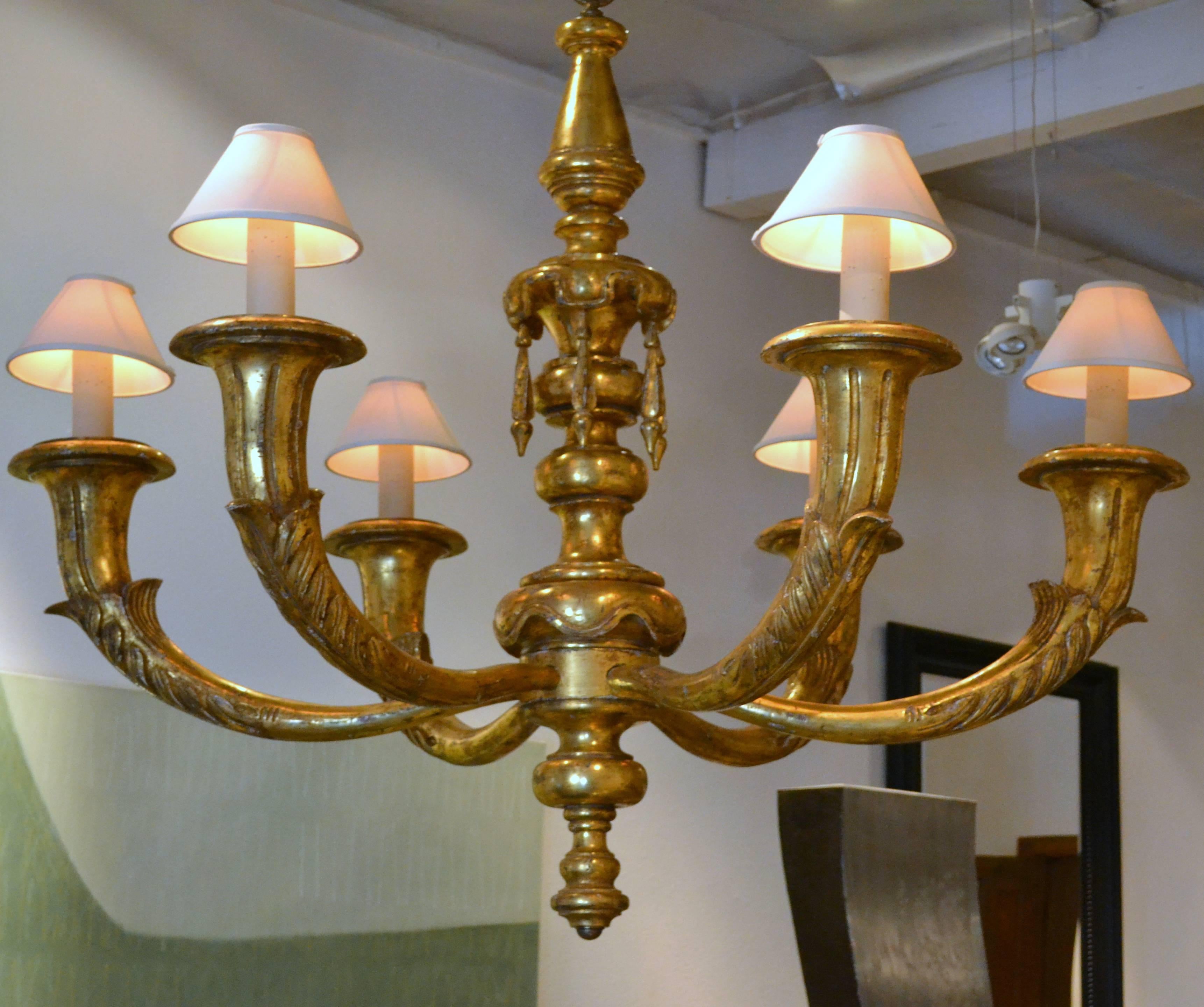 The mere size of this absolutely impressive giltwood chandelier will attract your attention. It is a six-arm giltwood chandelier with giltwood hanging tassels. The faux candlesticks are shielded with ivory fabric shades. The chandelier measures over