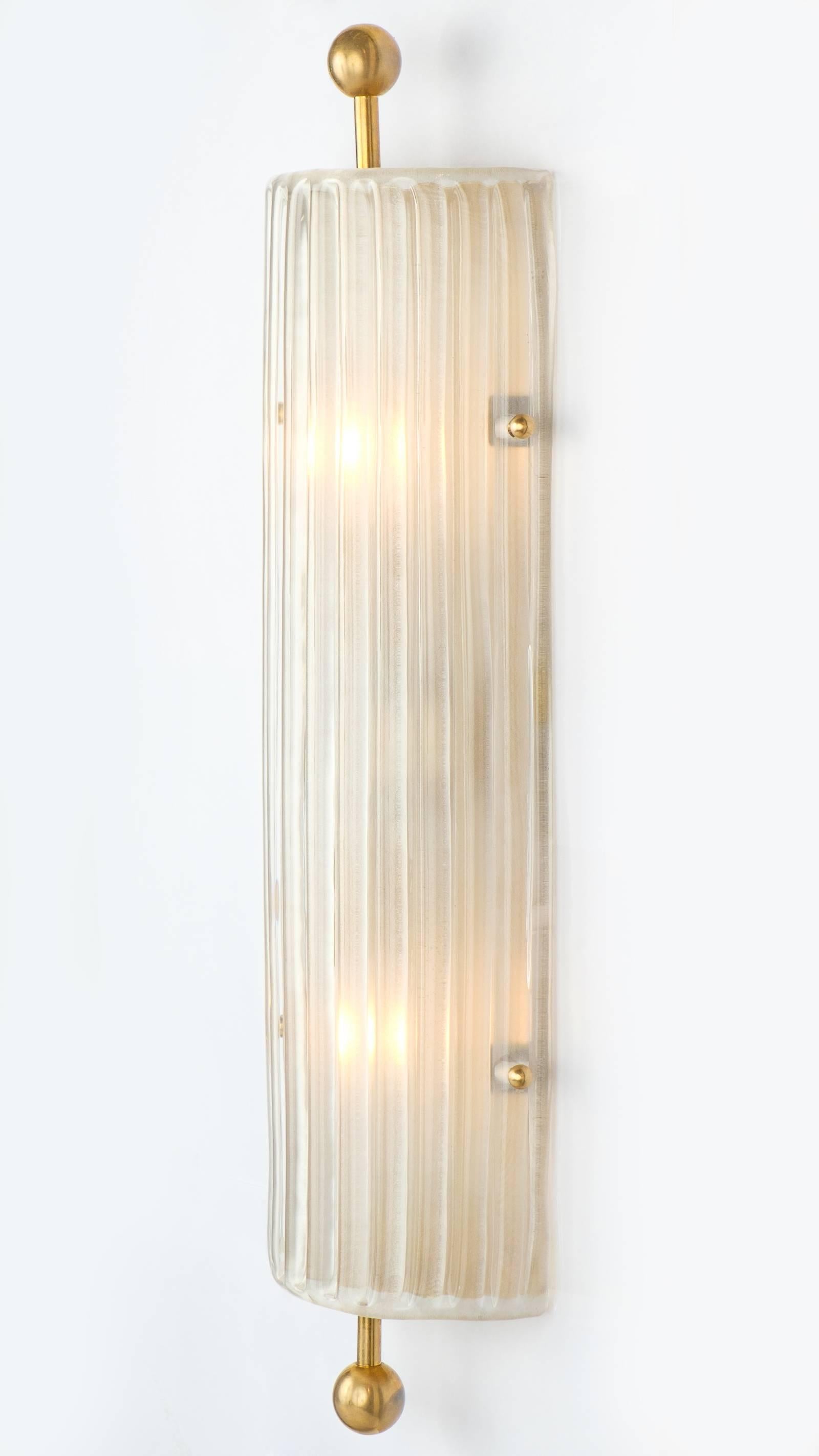 A pair of elegant elongated Art Deco style Murano glass and brass finial sconces. These flush mount lighting pieces have a timeless structure that is taken up a notch via the ribbed, textured, and frosted Murano glass. Each sconce requires two