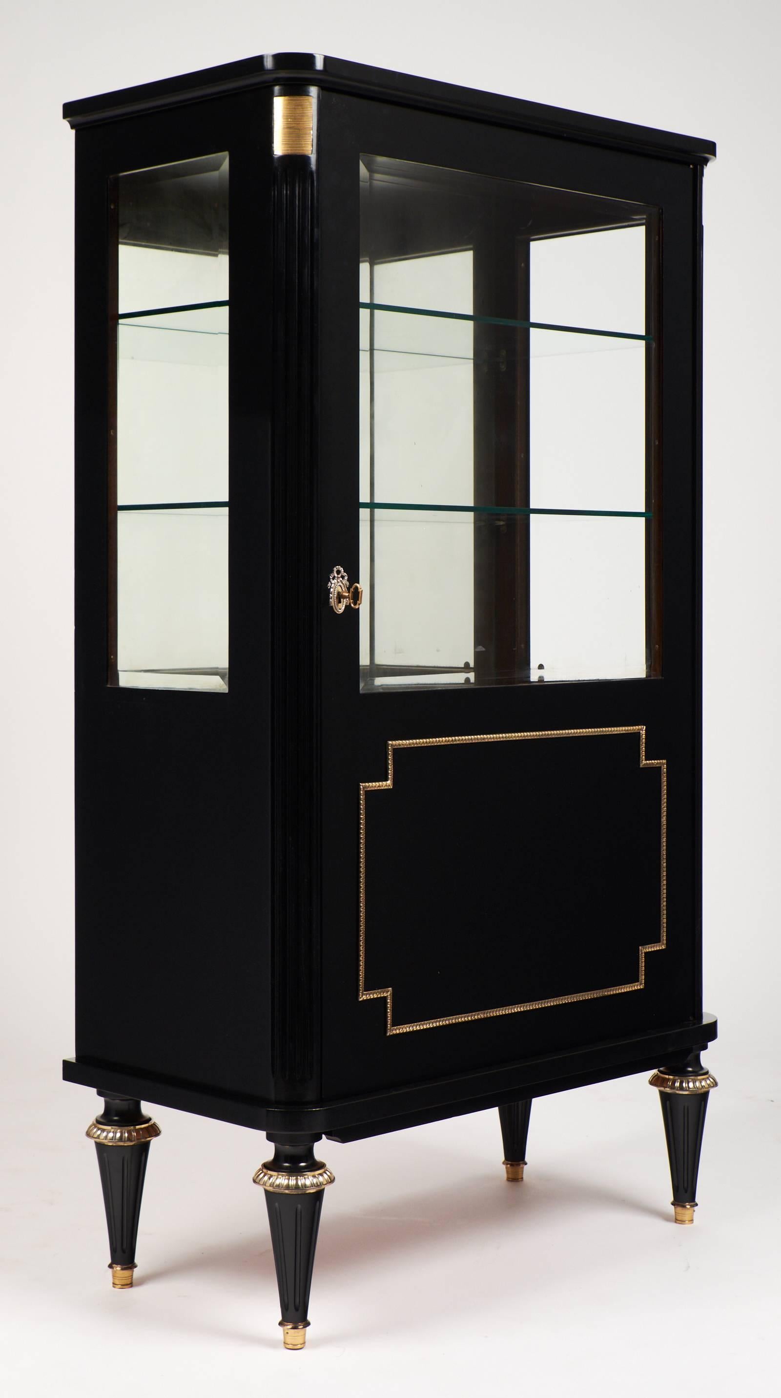 French mahogany bookcase in the manner of Maison Jansen, circa 1940. Beveled glass doors and sides, mirrored back with gilt brass details, capped feet, and trim.