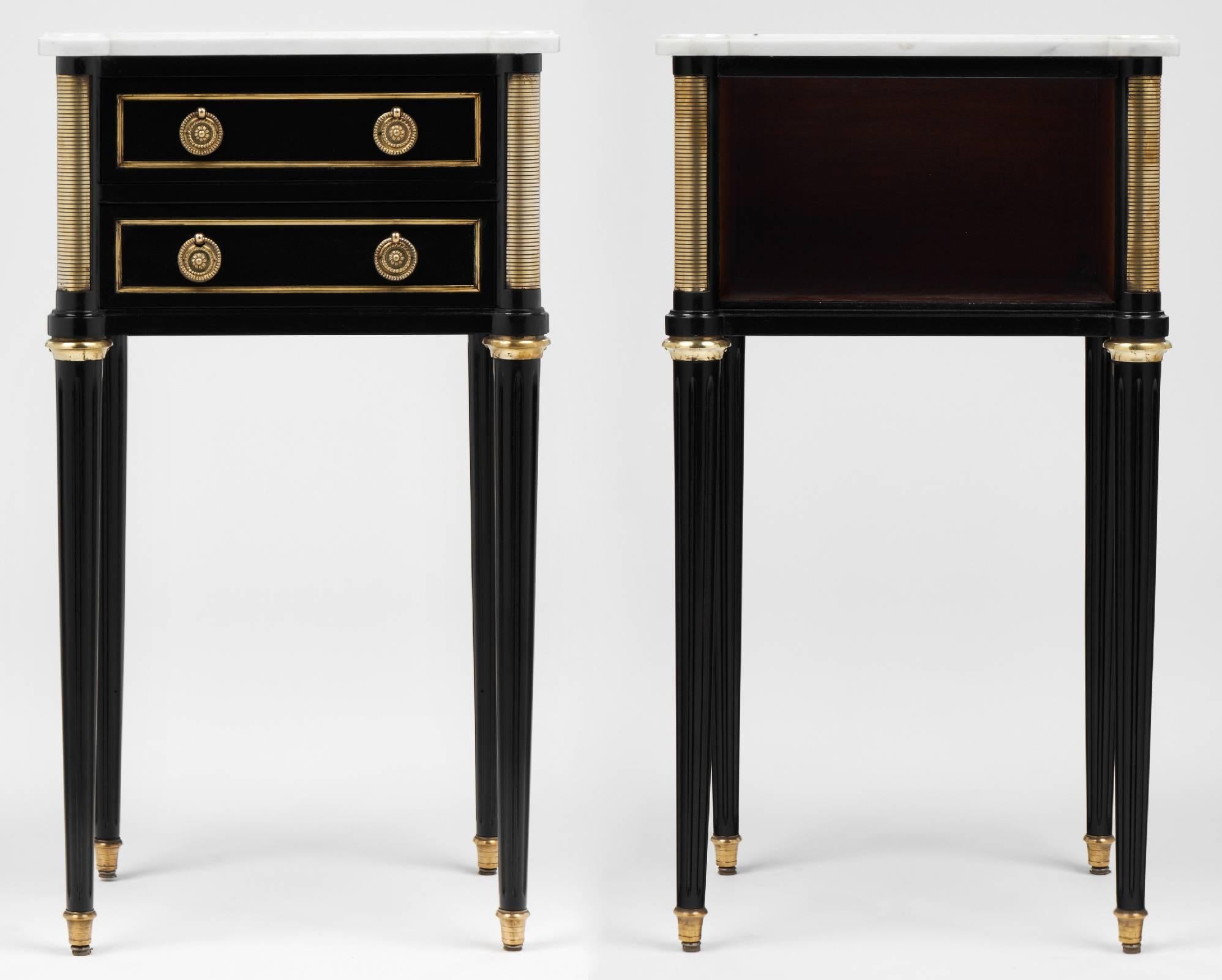 French vintage pair of nightstands in the classic and elegant style of Louis XVI, with clean lines, polished style, and tapered legs. Pristine Carrara marble tops and gilt brass trim gleam against black lacquered mahogany on this set of side tables.
