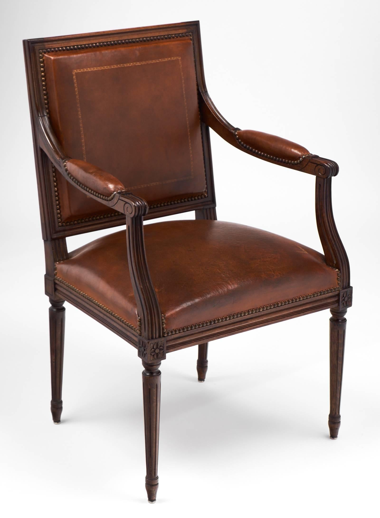 French Louis XVI style armchair of solid, fluted cherrywood. Original leather upholstery is embossed with gold leaf and studded with brass tacks. The arm height is 28.25