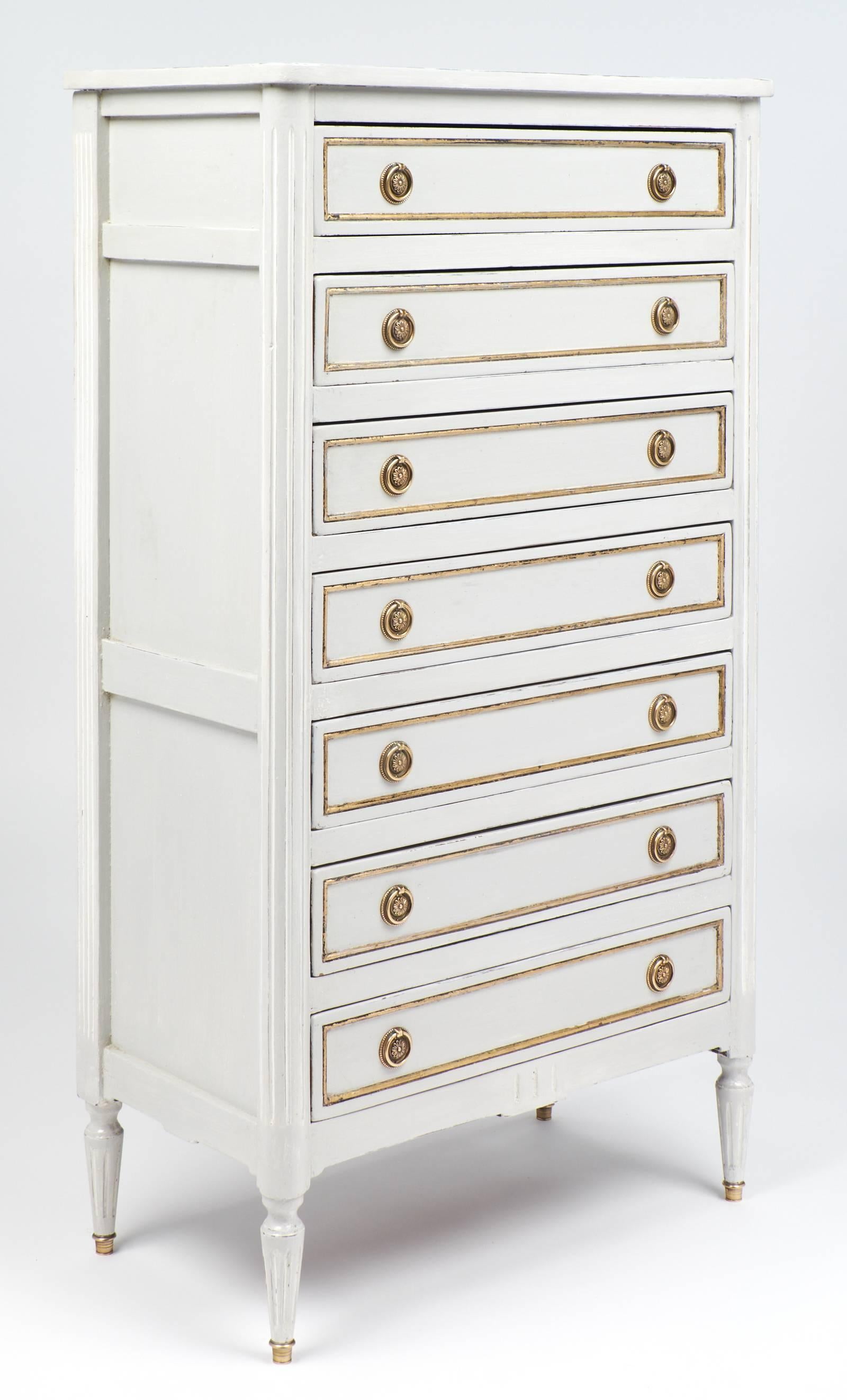 Antique French semainier chest of drawers painted dove grey and featuring brass hardware and gold leaf detailing on each drawer. This piece includes seven dovetailed drawers, giving it the name semainier. In French, semaine means week; one drawer