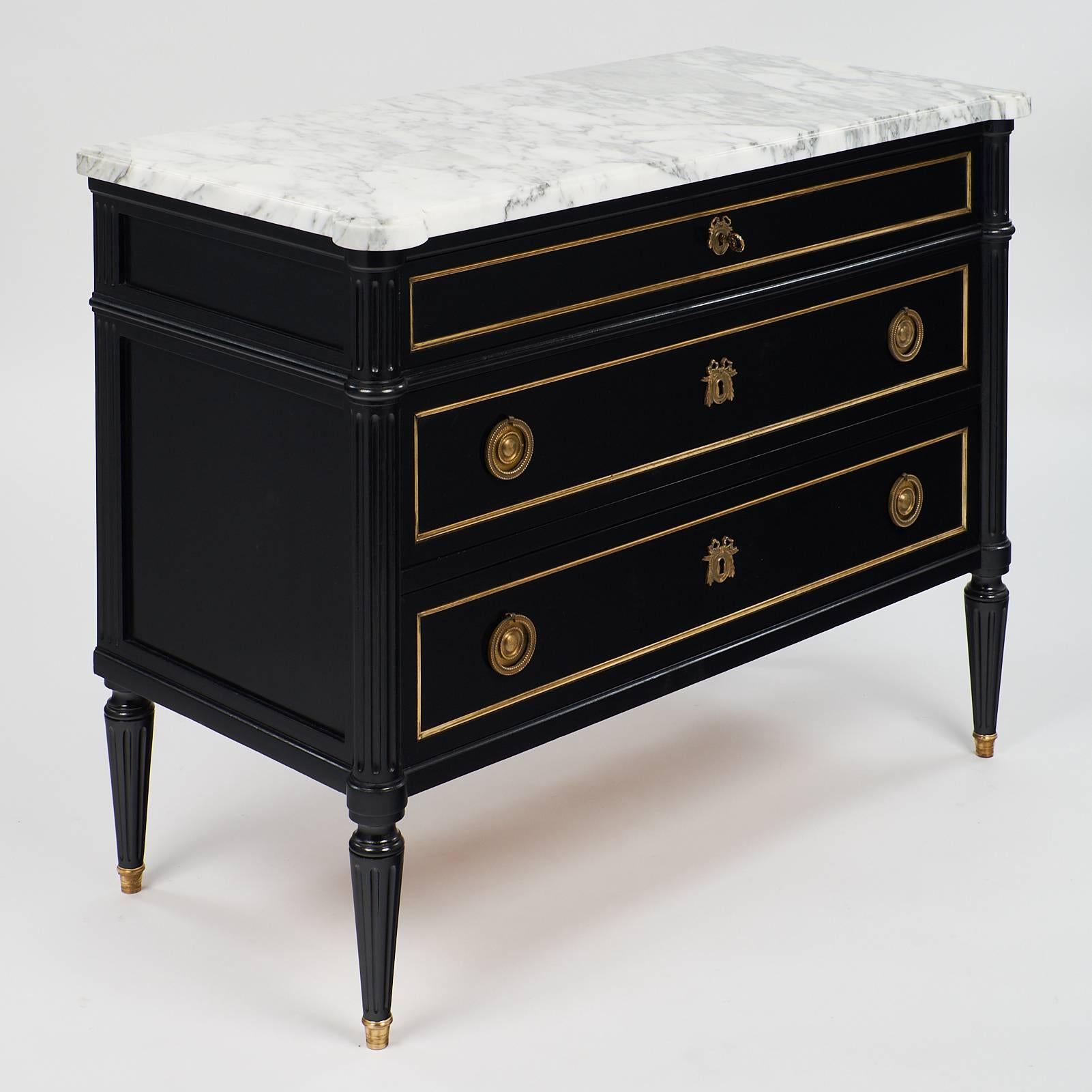 This Classic Louis XVI style ebonized chest features a stunning Carrara marble top with rich veining, three dovetailed drawers, and tapered, fluted legs, circa 1890. This beautiful piece has brass trim and feet caps, as well as beautifully cast