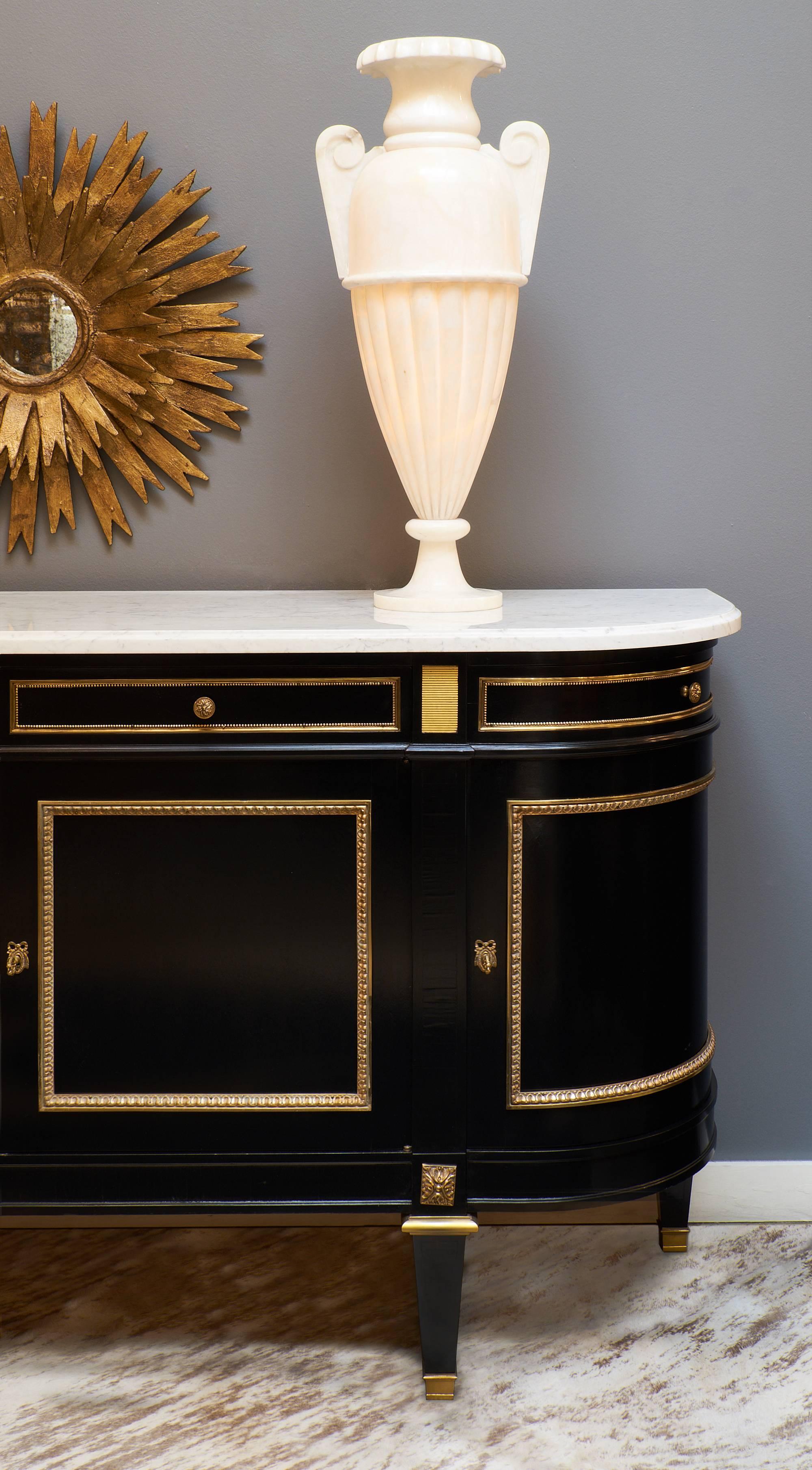Ebonized grand buffet/enfilade made in the Louis XVI style. This mahogany piece is finished with a museum quality, lustrous French polish and has an intact and subtly veined Carrara marble slab original top. Gilt brass trim and ormolu details give