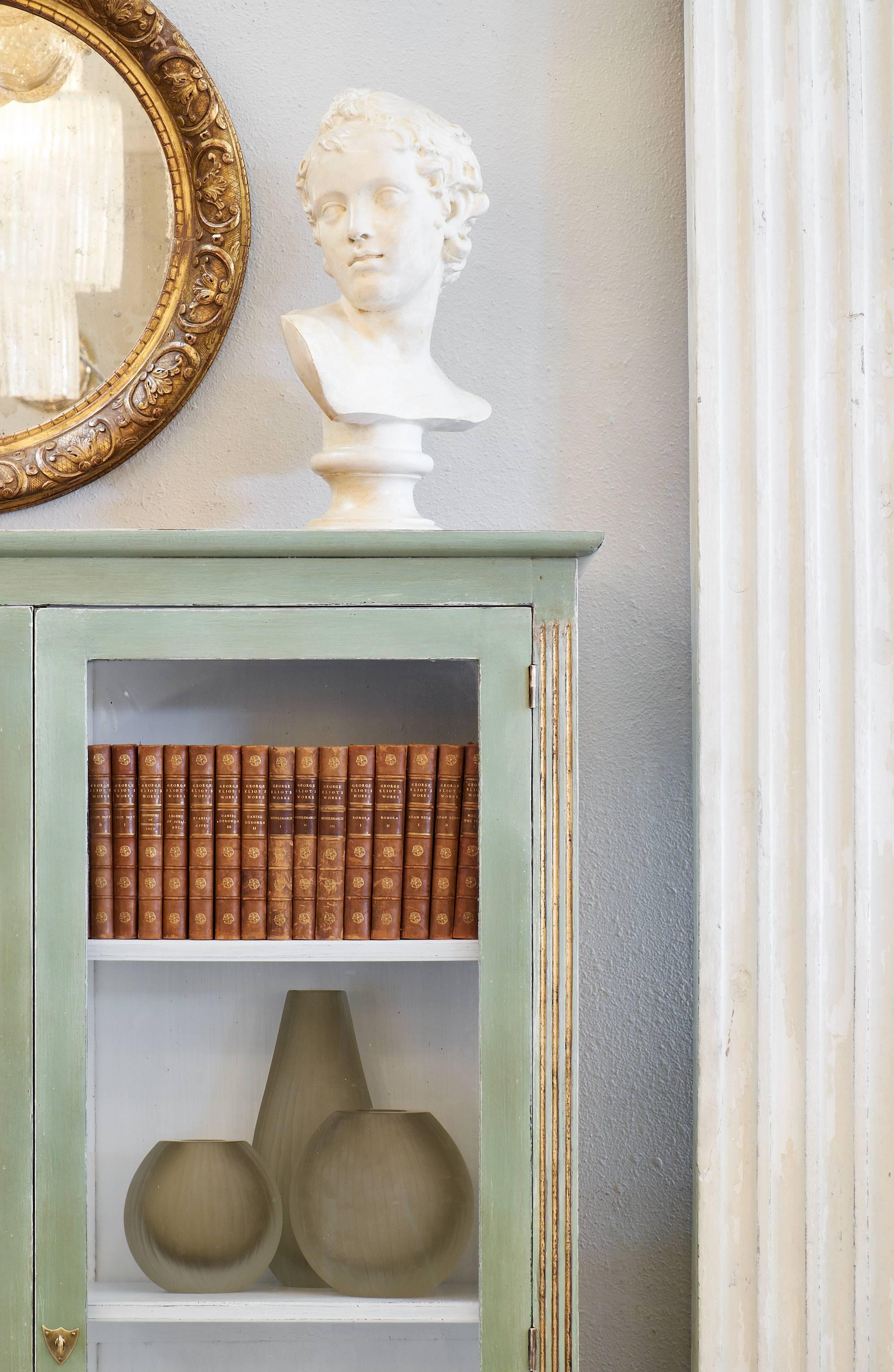 Louis XVI style bookcase of painted mahogany with gold leafed accents and fluting on the sides. This French antique piece has glass doors. Three adjustable shelves make this an efficient addition to many settings! This bookcase is a versatile and