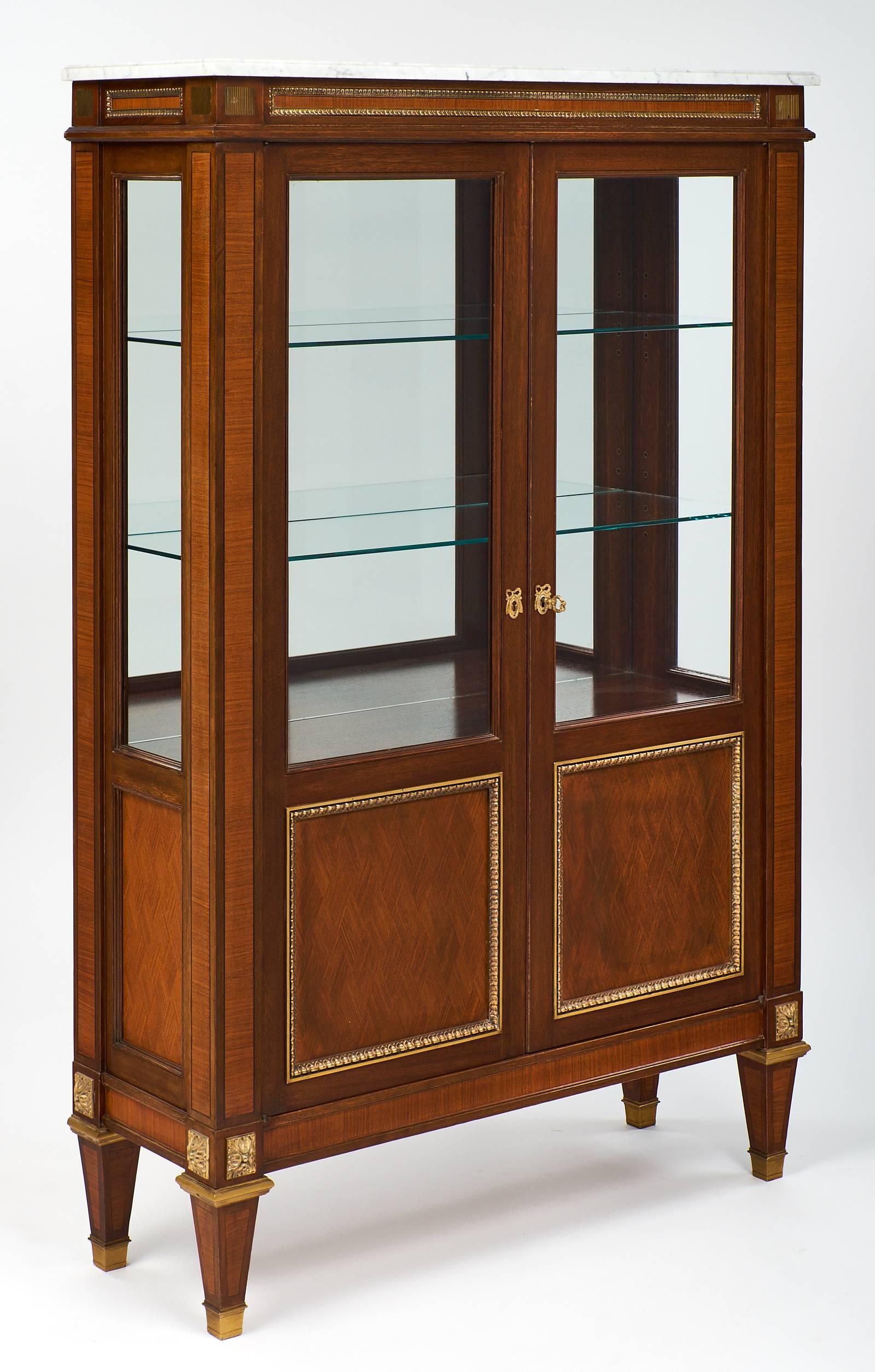 Louis XVI style bookcase with refined and elegant rosewood parquetry, marquetry, and tinted rosewood and burled ash on the panels. This piece has finely cast ormolu, feet, and trims, as well as a wonderful Carrara marble top. This vitrine has a