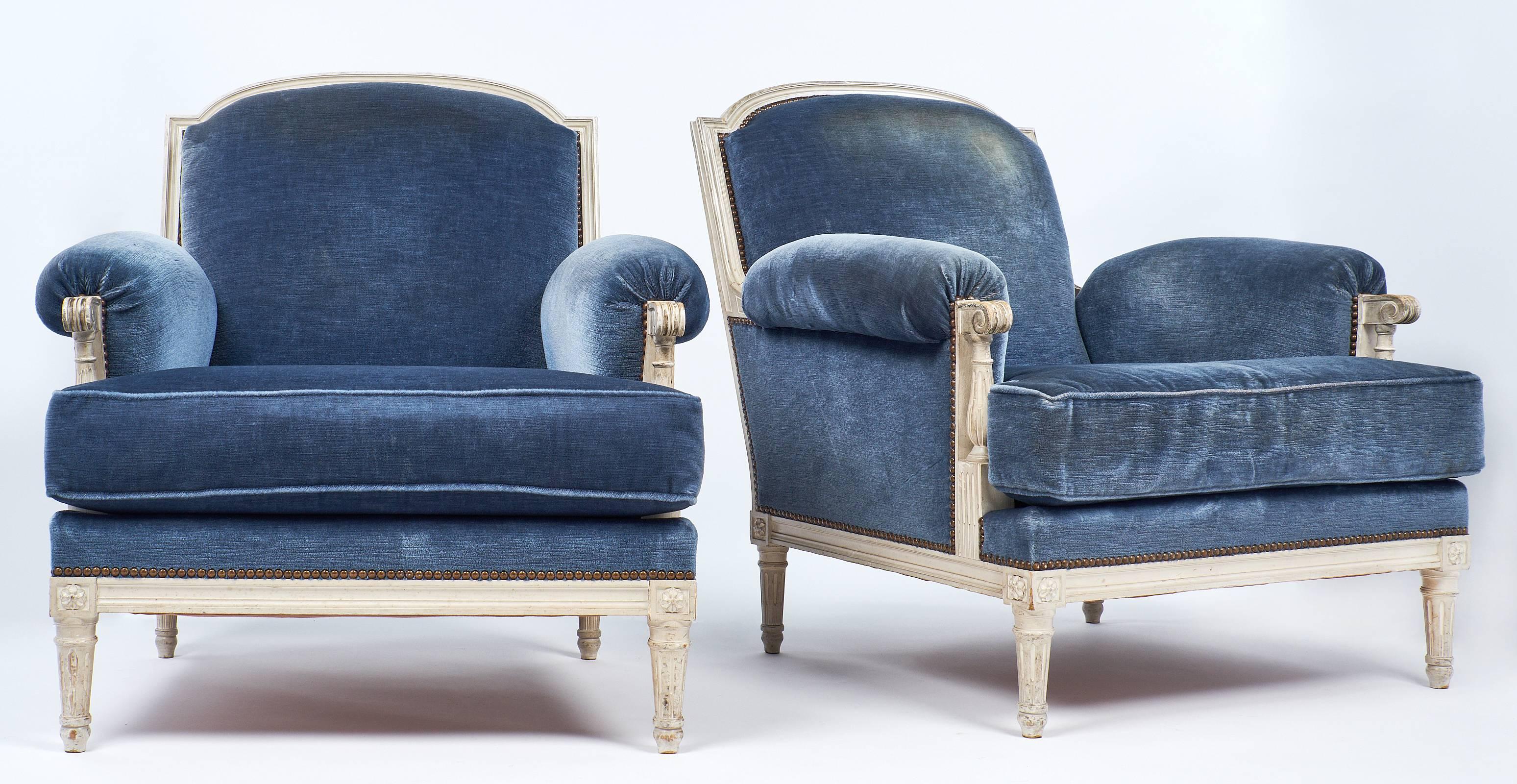 French antique Louis XVI style bergères made of painted and patinated beech wood with hand-carved designs. The blue velvet is in decent condition. These chairs are very comfortable and strong! 

