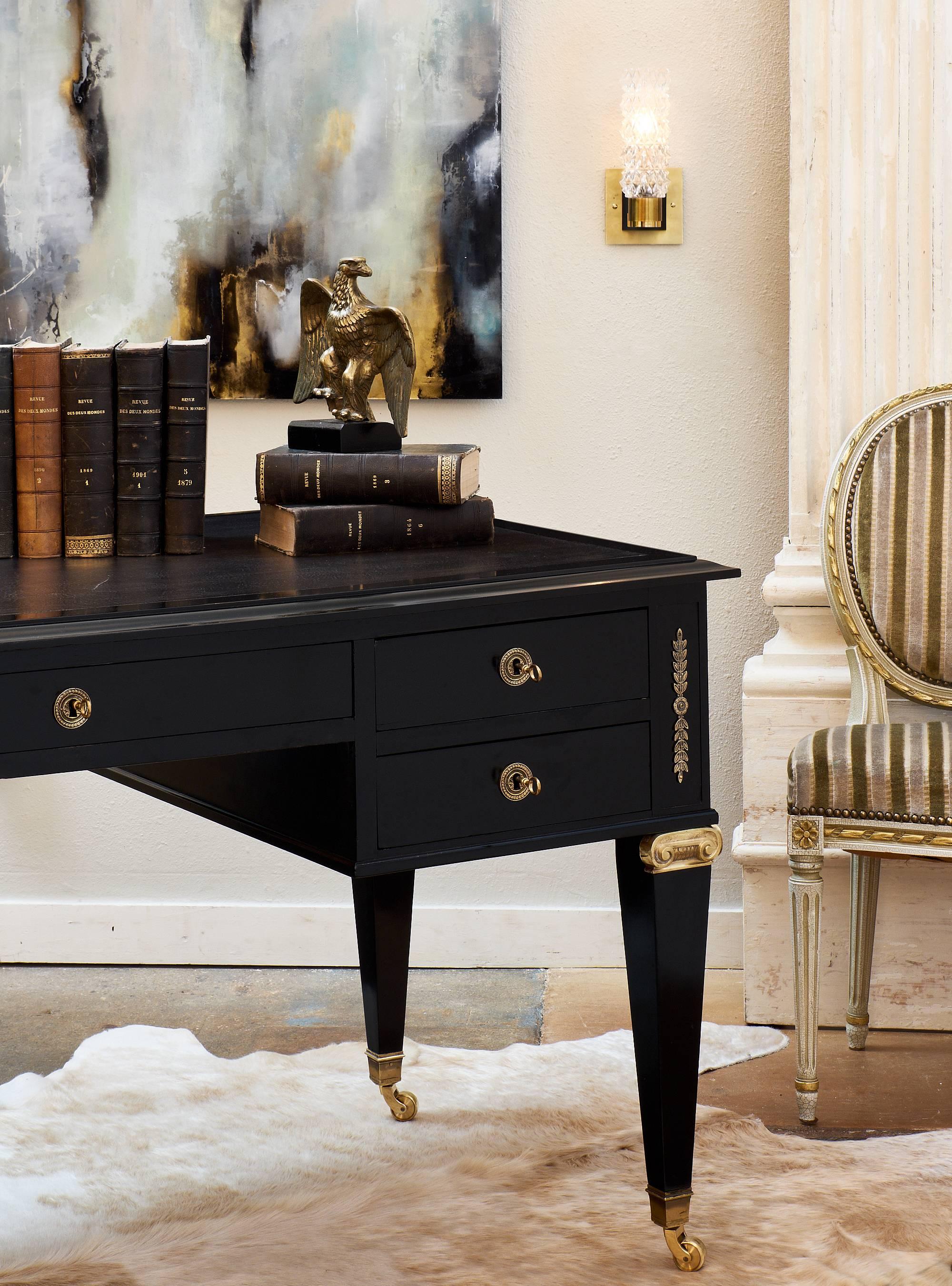 Wonderful Directoire style antique French desk with rich ormolu decor of foliage and scrolls, casters, and a black leather top. The superb museum quality French polish finish brings luster to the ebonized mahogany piece. Working locks and original