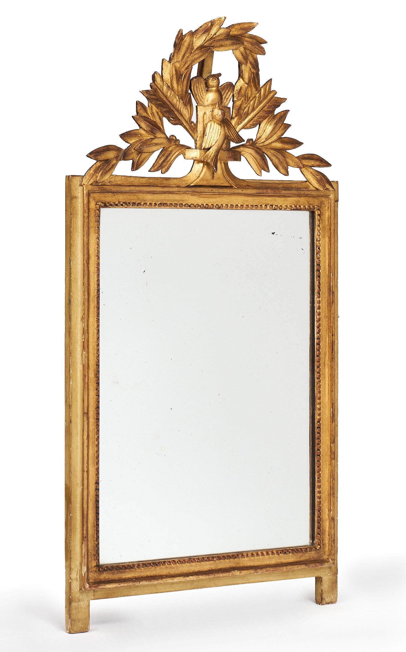 French Louis XVI style mirror with a charming 23-karat gold leaf finish. The frame is hand-carved wood composition of foliage, arrow, and bird. This decoration and style are typical of the neoclassical period. The mercury mirror is