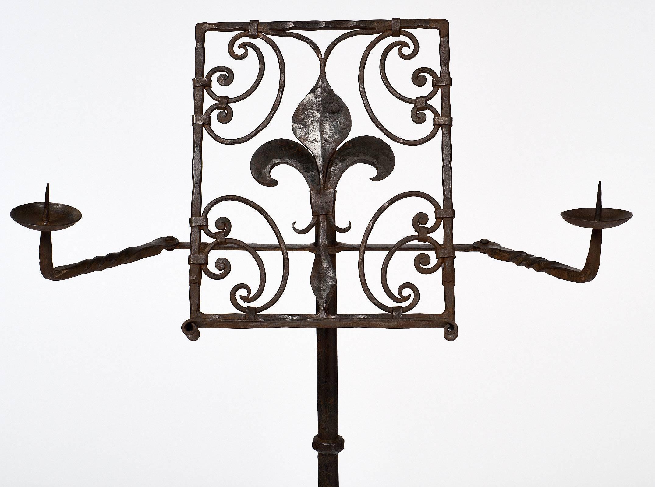 Hand-hammered French antique lectern in the Renaissance style from the 19th century. This forged iron piece is decorated with a fleur-de-lys and has two adjustable arms with candle holders. There is a tripod base on the bottom. This lectern is very