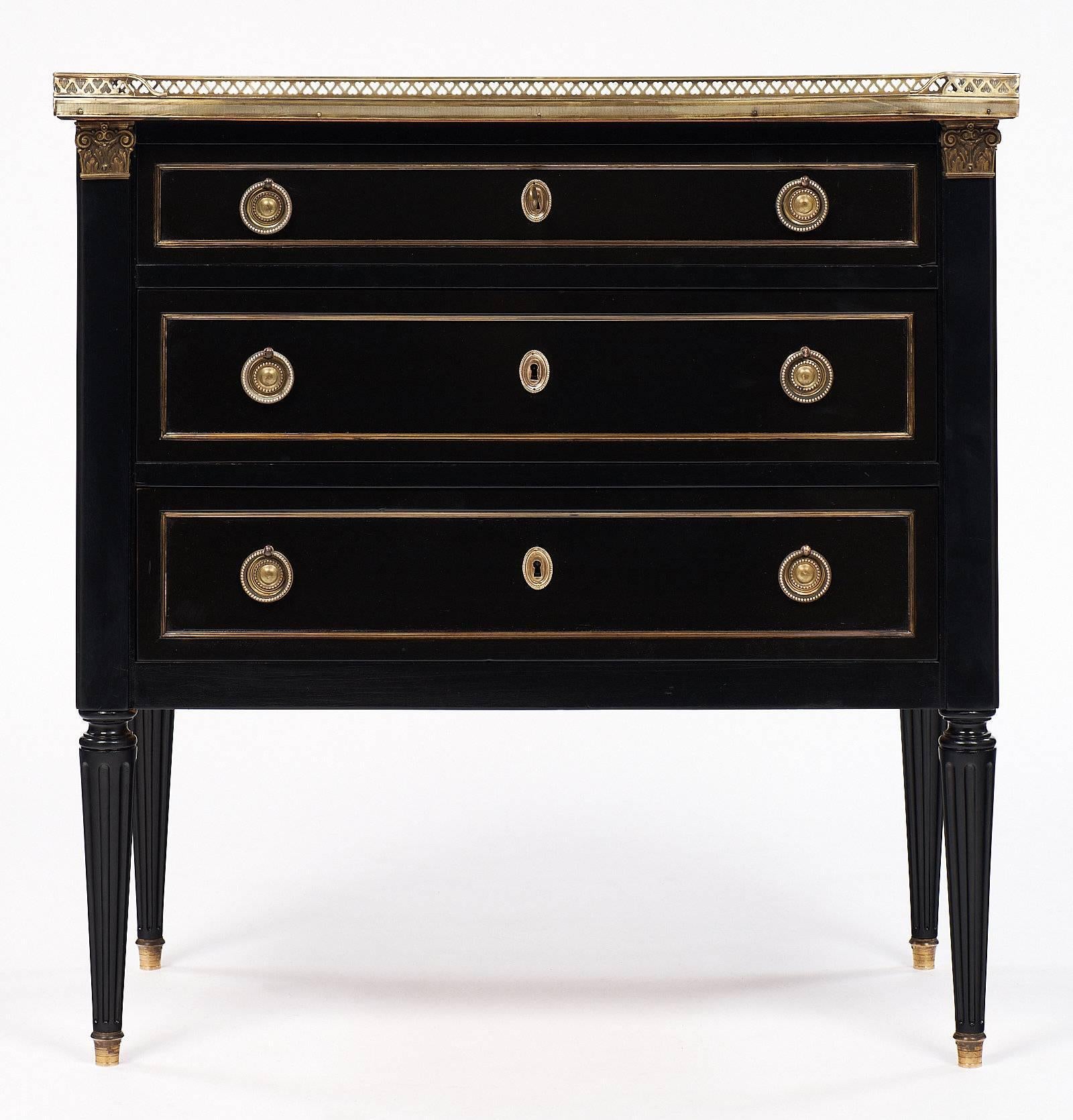 Louis XVI style antique chest from France with an opened brass gallery and Carrara marble top. This mahogany piece has been ebonized and finished with a French polish for luster. This chest also features finely cast hardware and gilt brass trims.