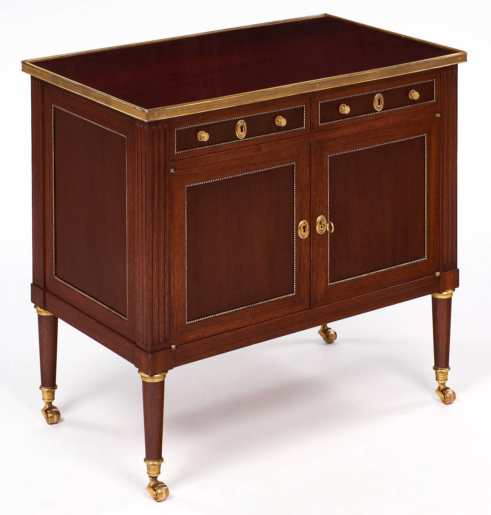 A very fine mahogany chest on solid gilded brass casters in the Louis XVI style. This small case piece rests on tapered legs with gilt brass trims. The hardware and trim throughout are also brass. There are two small drawers above two doors. We