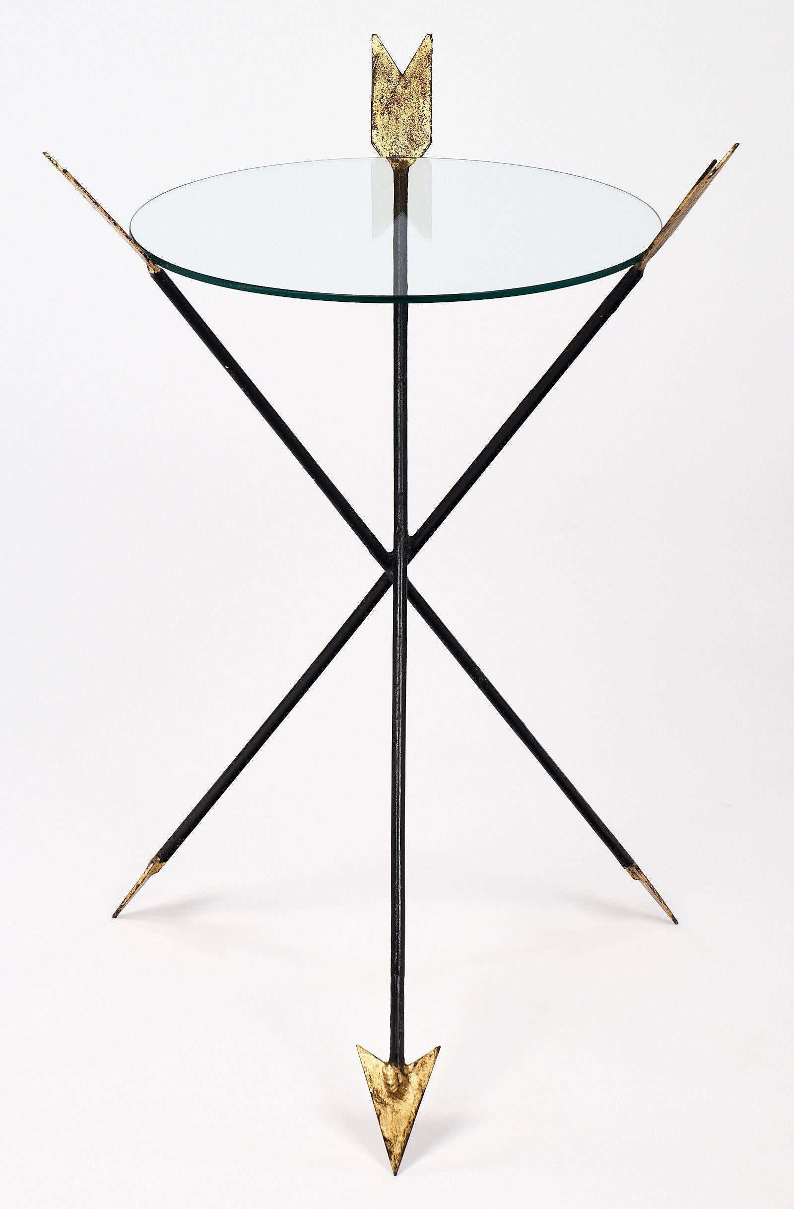Empire style side table made of forged iron with lots of charm. This lovely piece has three arrows overlapping to create a tripod base. The arrows are made of iron and the tips and ends are gold leafed. A circular glass top fits between the arrows.
