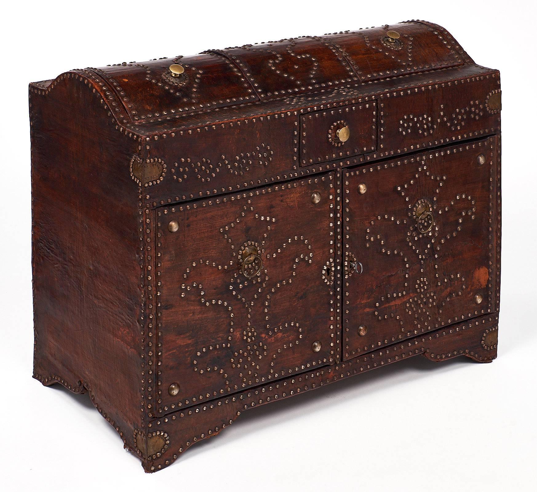 Beautifully intricate wooden trunk wrapped in Moroccan leather and adorned with beautiful designs make of brass studs. This piece has two compartments on top that lift open, as well as two doors on the front for storage. The interior is lined with