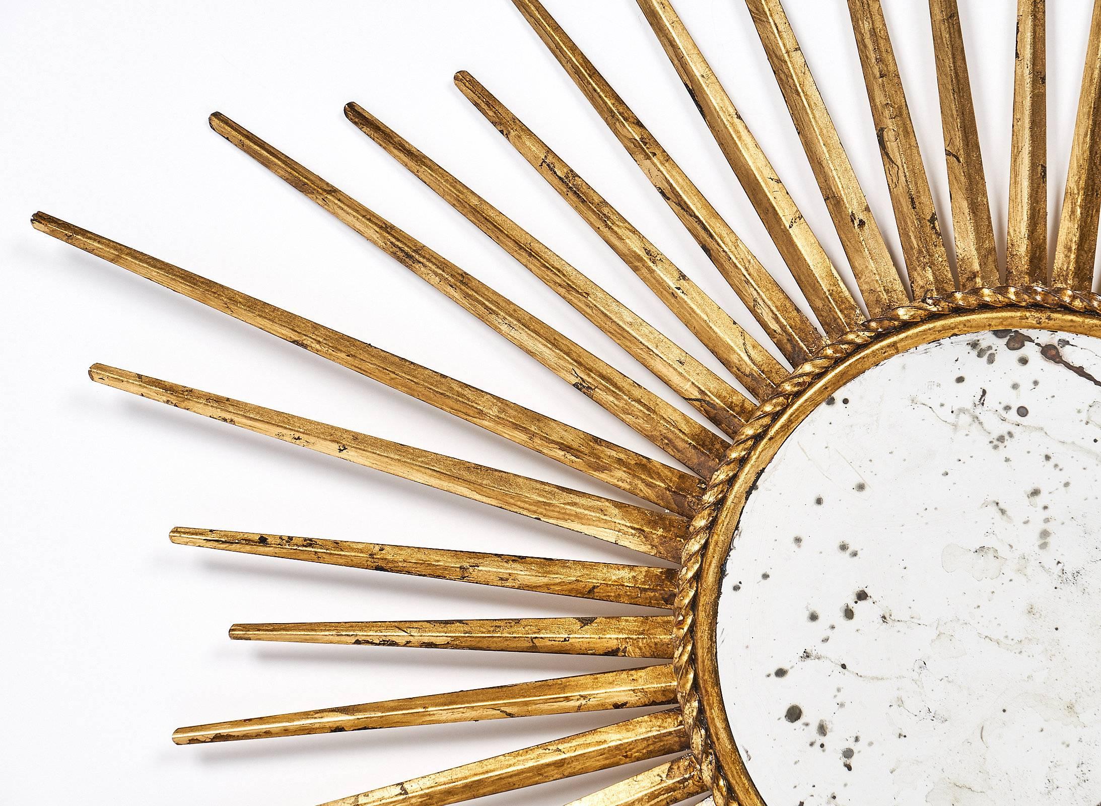 Sunburst shape mirror made of gilded metal and featuring an antiqued mirror as the center. This delightful French piece in the Mid-Century Modern style is the perfect size for a bedroom or entryway, and the thin rays give it high impact. We love the