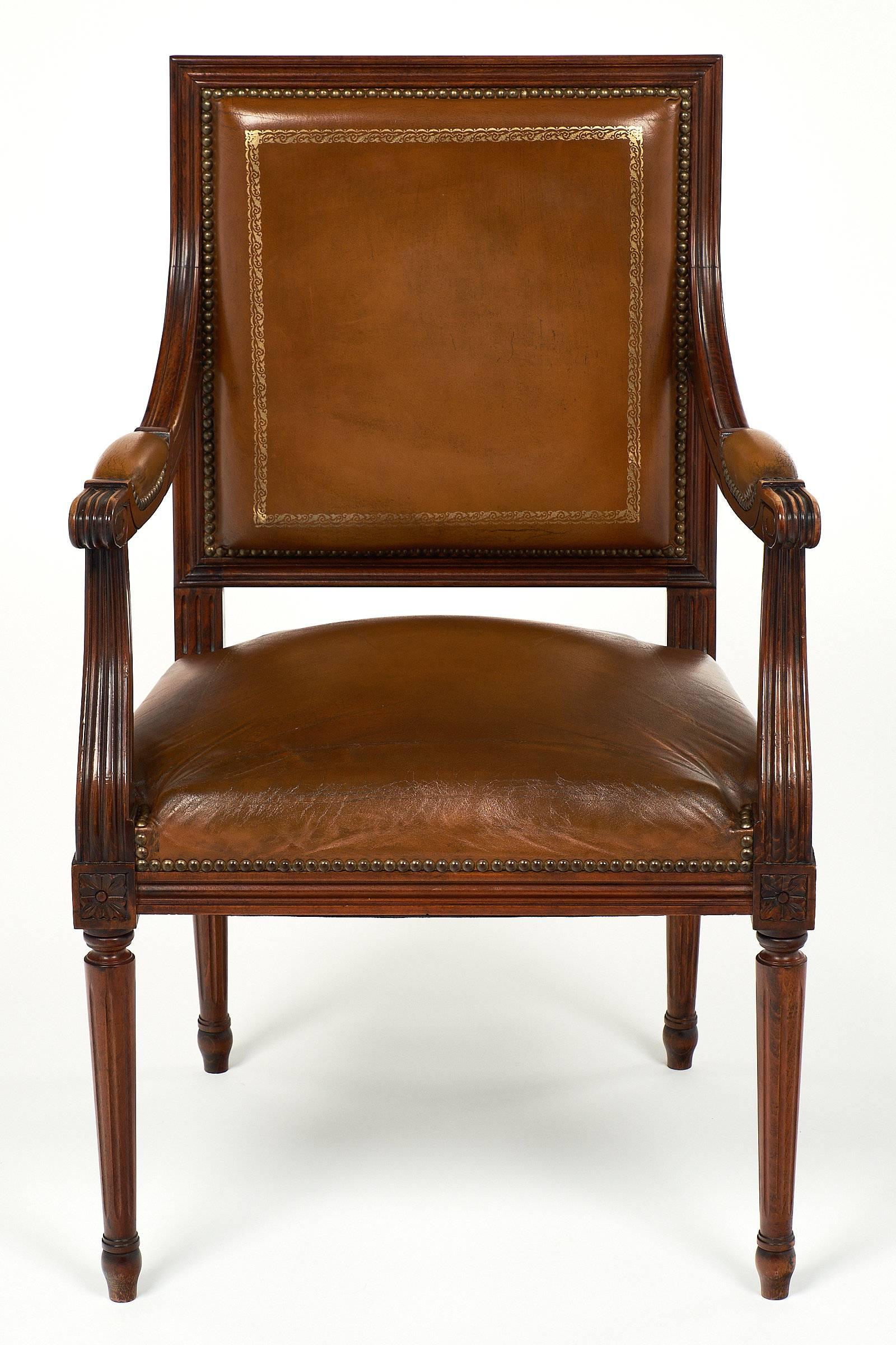 Handsome armchair in the Louis XVI style. This piece has a hand-carved and fluted mahogany frame with beautiful scroll details on the arms. The four legs are fluted and tapered. The chair has the original leather upholstery with gold-leaf frieze